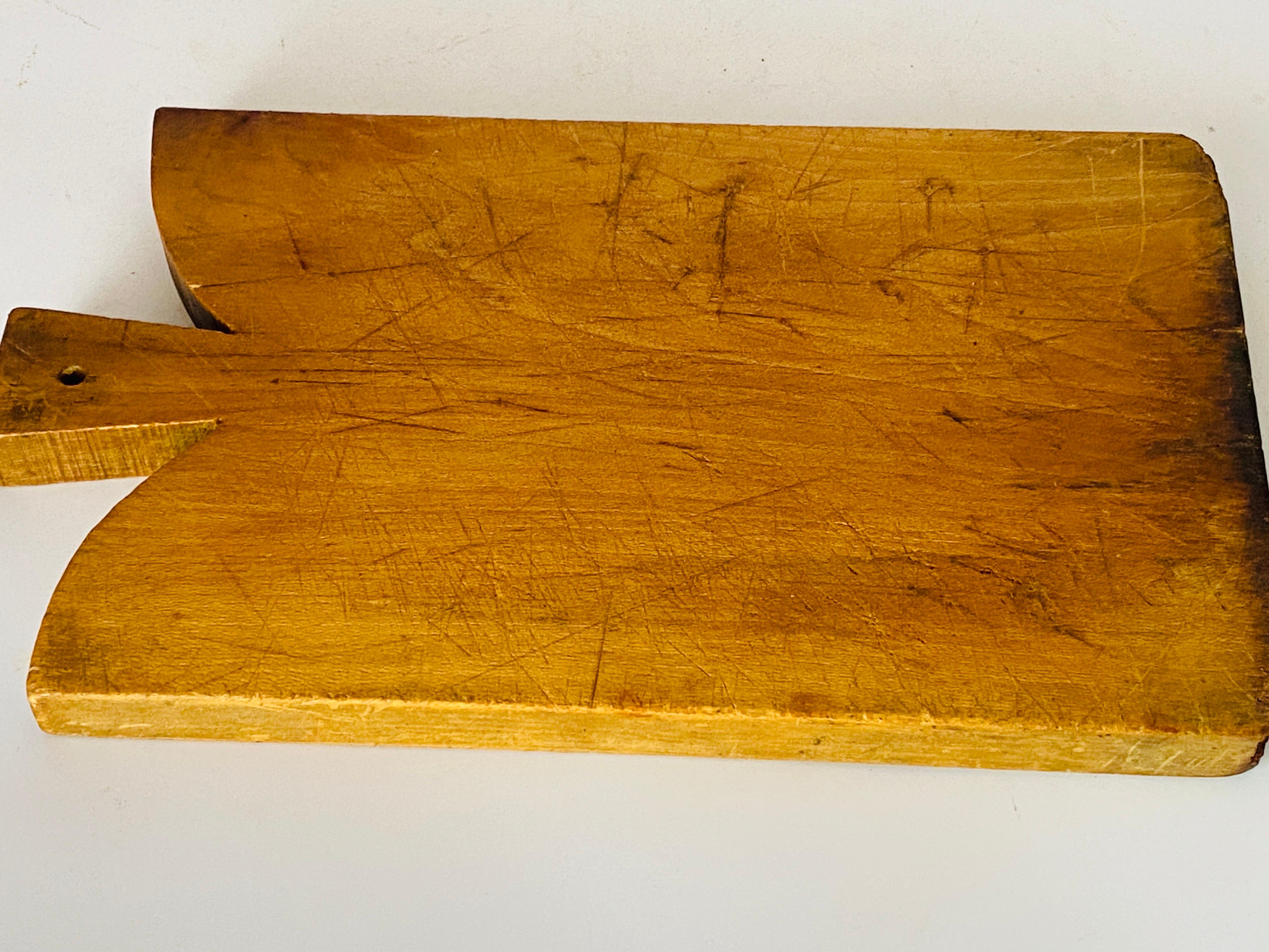 Planche à découper en bois, avec sa patine ancienne. Il s'agit d'un objet du XXe siècle français, dans le style French Provincial de couleur brune, et dans un état correspondant à son âge et à son utilisation.