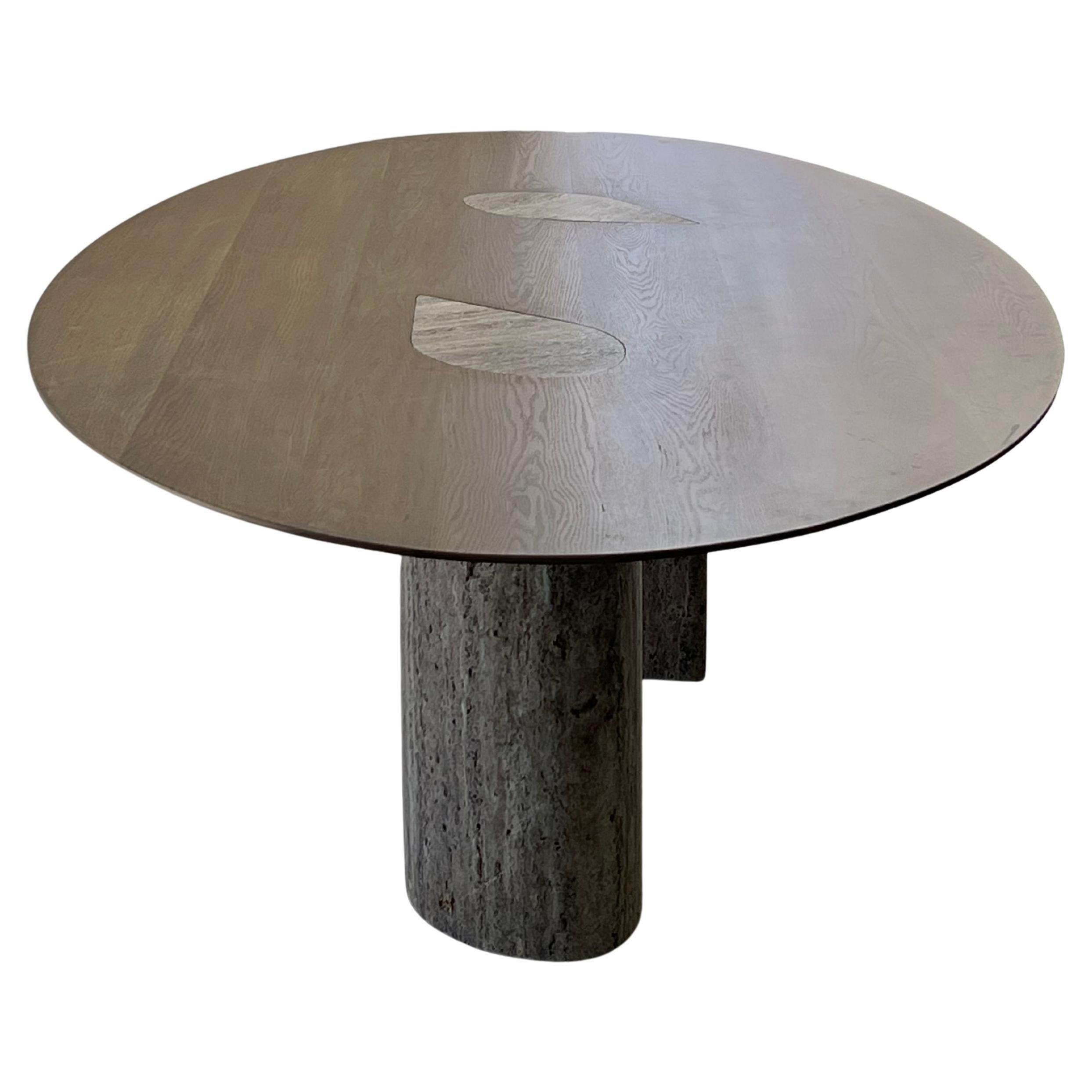 Cutting Corners is a travertine & wood dining table, designed to celebrate curvaceousness while maintaining the minimum possible footprint.

It consists of an oval surface in oak supported by two thin but sculptural legs, which take up a different