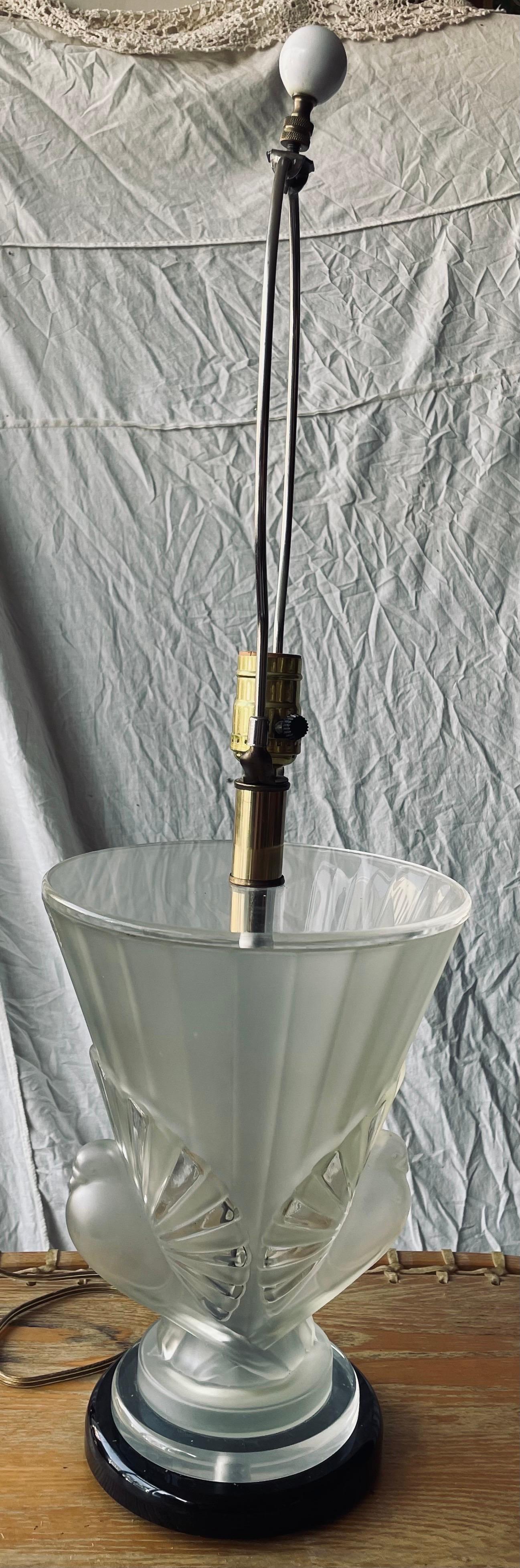 This is a fantastic art deco style mid century modern frosted Lucite table lamp in the shape of an urn sitting on a black base with figures of birds, tails splayed, alternating clear and frosted feathers, on either side. I think the birds are