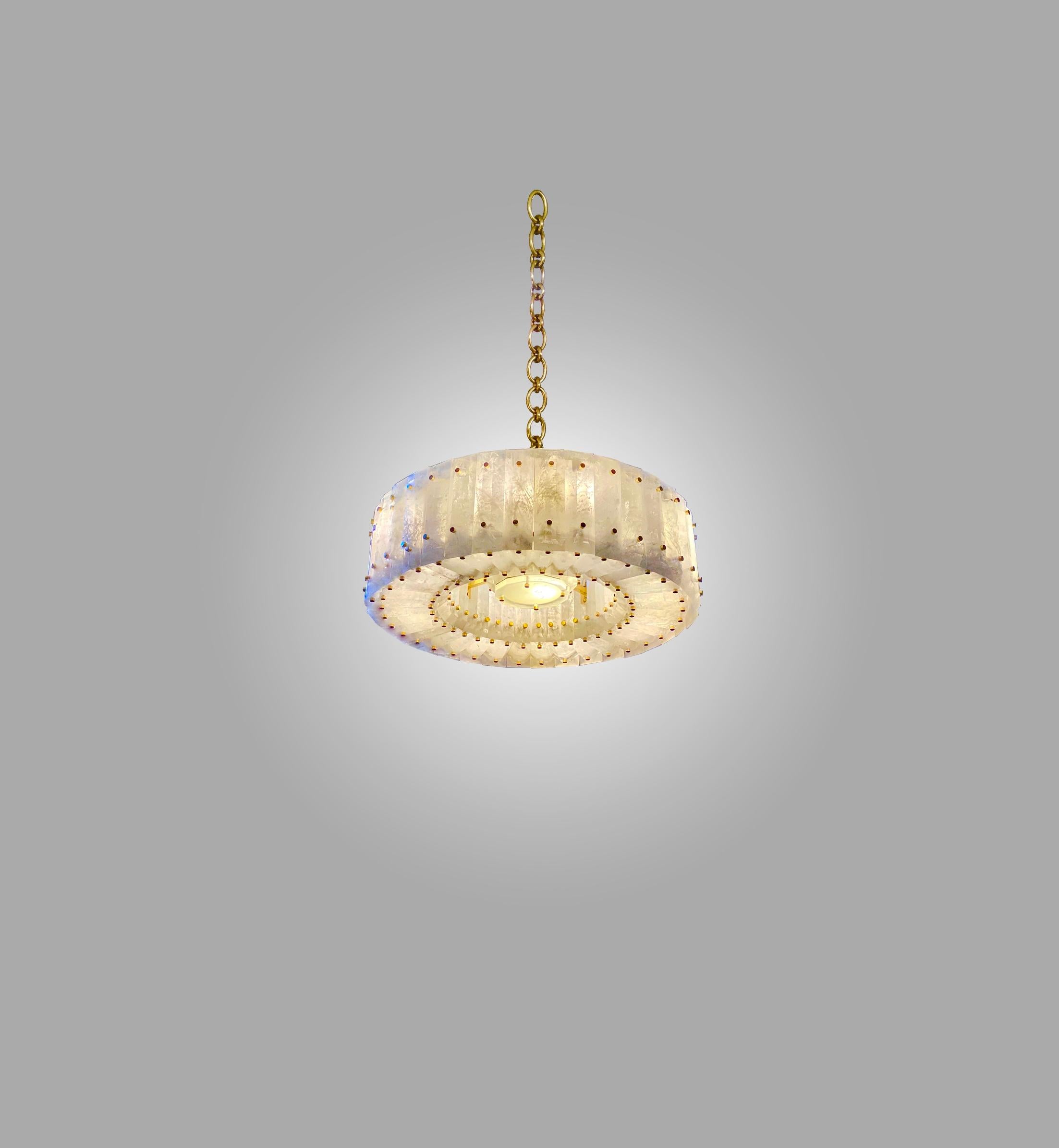 Round rock crystal chandelier with center section and brass nail decoration. Finely carved, multi-faceted rock crystal panels installed around the circumference of the circle. Hung from a finely cast polished brass chain. 
Overall height can be