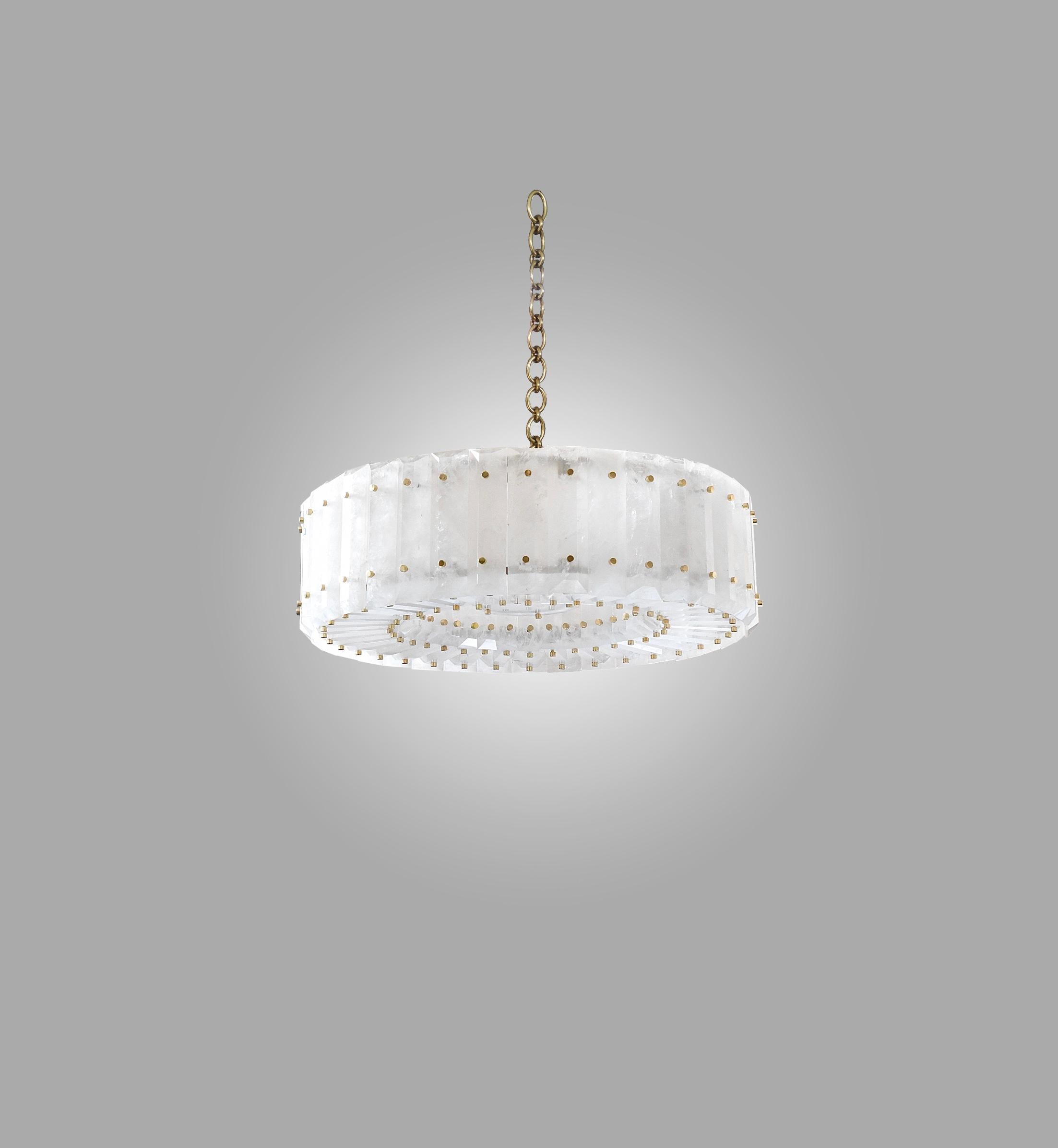 Round rock crystal chandelier with center section and brass nail decoration. Finely carved, multifaceted rock crystal panels installed around the circumference of the circle. Hung from a finely cast polished brass chain. Overall height can be