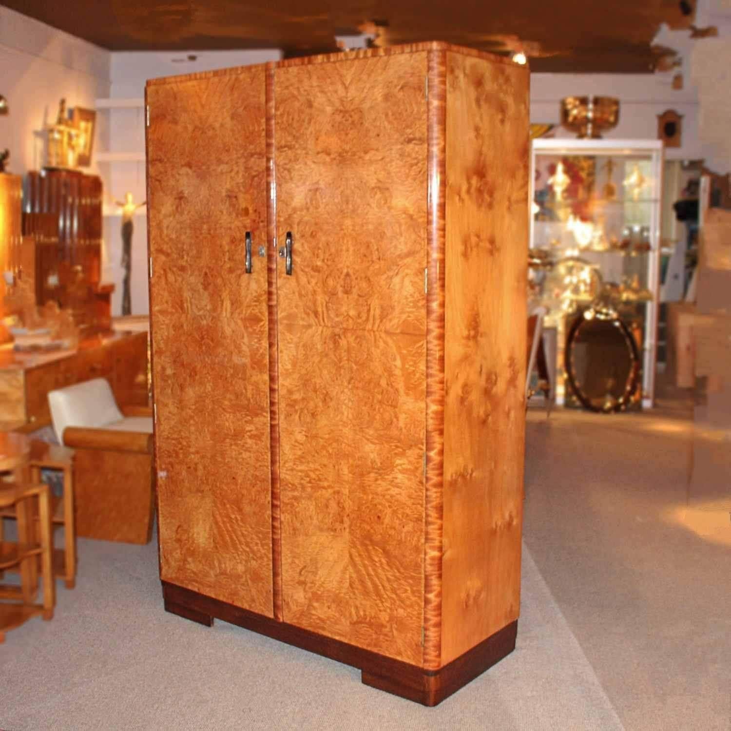 An Art Deco double wardrobe in burr satin wood, satin birch banding and figured walnut sides. Set over a stepped oak base. Original bakelite and metal handles with push button lock release. Interior with two separate handgun rails and original hooks