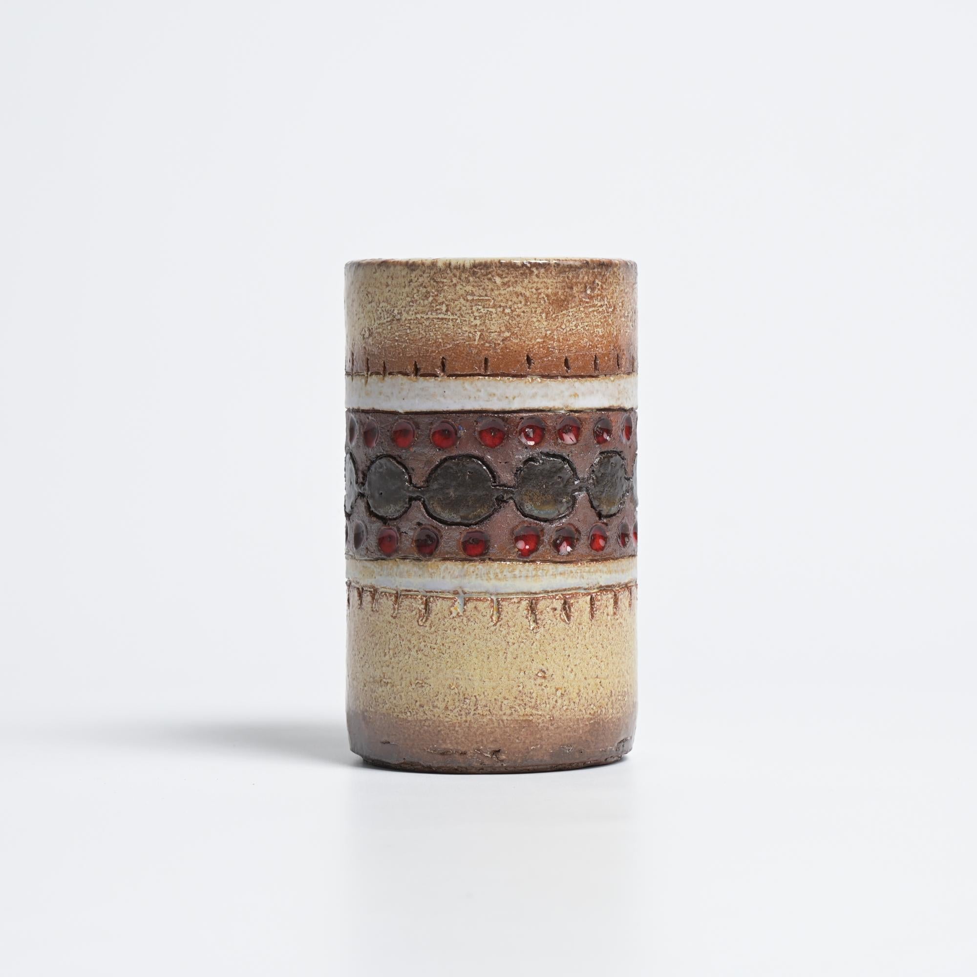 This cylindrical vase was crafted in the Perignem workshop in Beernem, Belgium. We date it back to the 1960s.

The vase has a glaze finish. The piece is complemented by round motifs with different glaze finishes and smaller, red accents.

The bottom