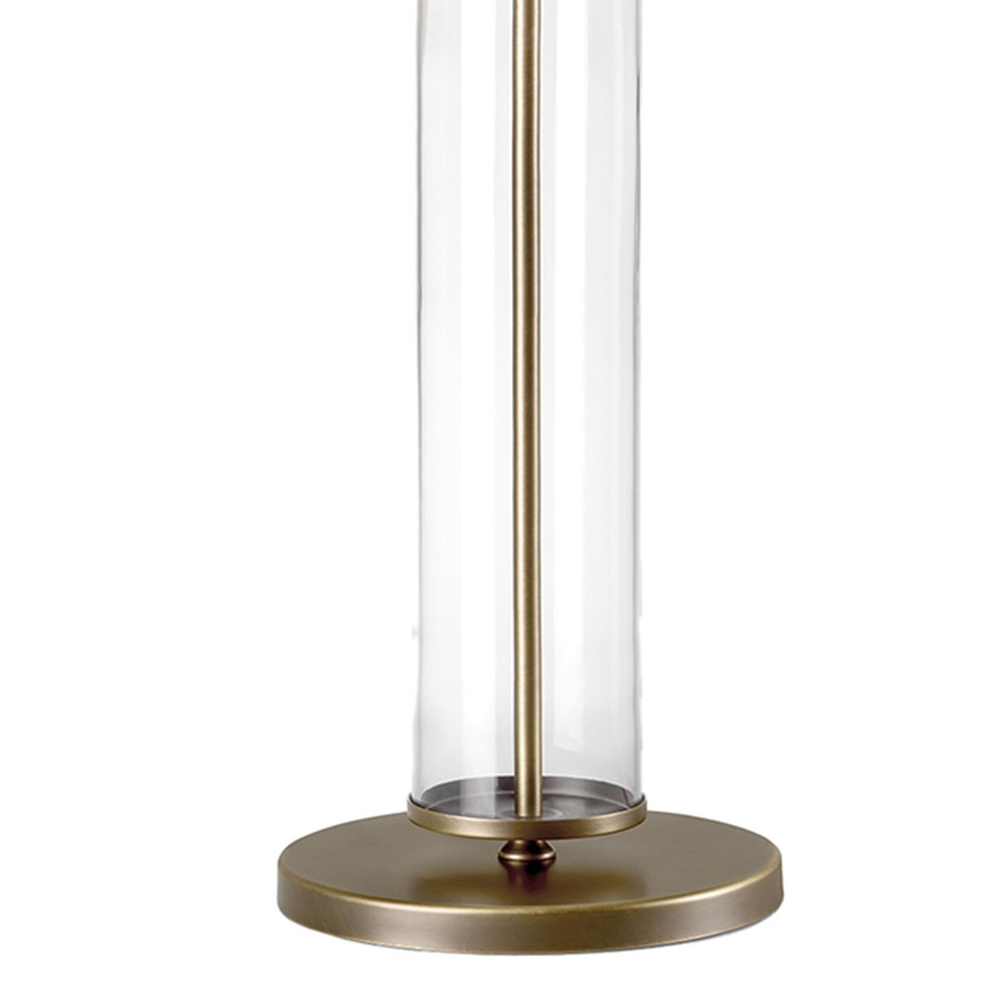 The Cylindra Table Lamp features an elegant design with a large fabric shade, a transparent central glass column, and a bronze-finished metal base. Measuring 40 cm in diameter and 76 cm in height, it delivers soft, diffused light ideal for living