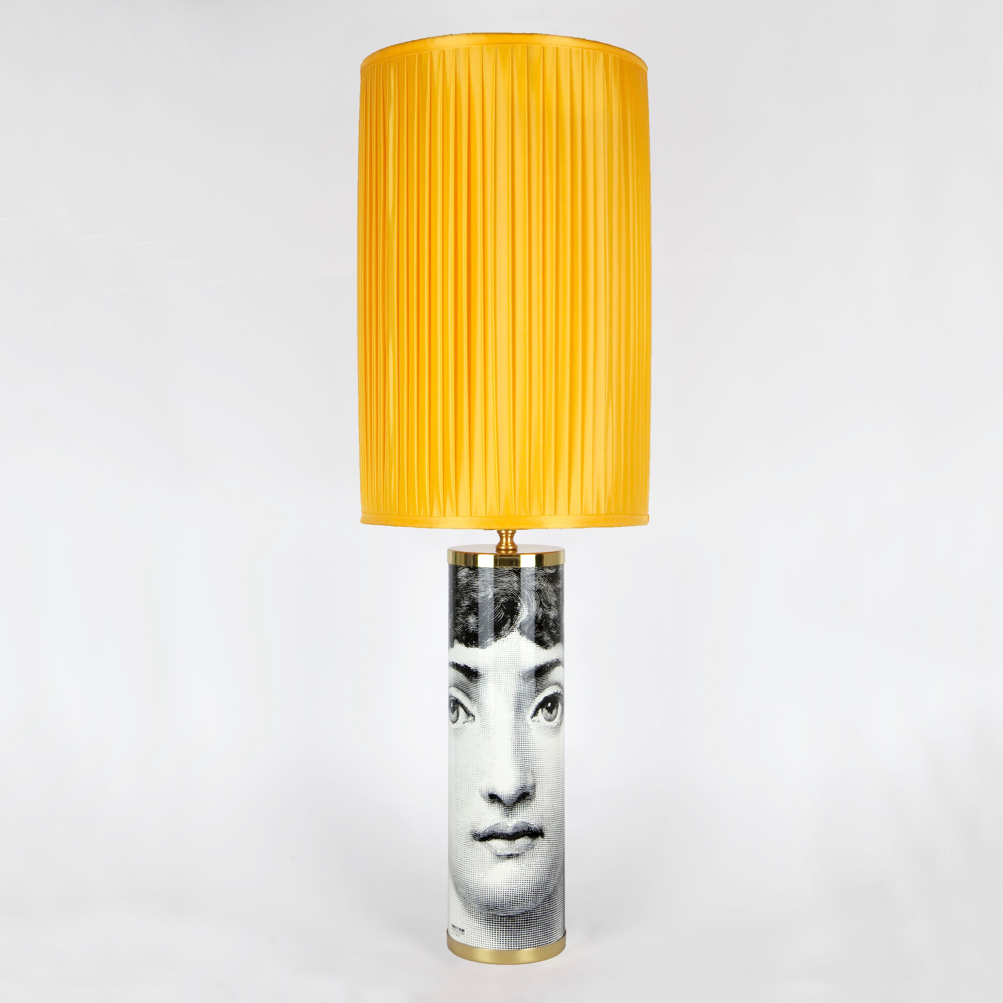 La forme cylindrique permet à l'imagination de Fornasetti de créer de surprenants effets décoratifs dans lesquels les formes se succèdent à l'infini. Le design du visage métafisque fait de cette base de lampe en métal sérigraphiée à la main un