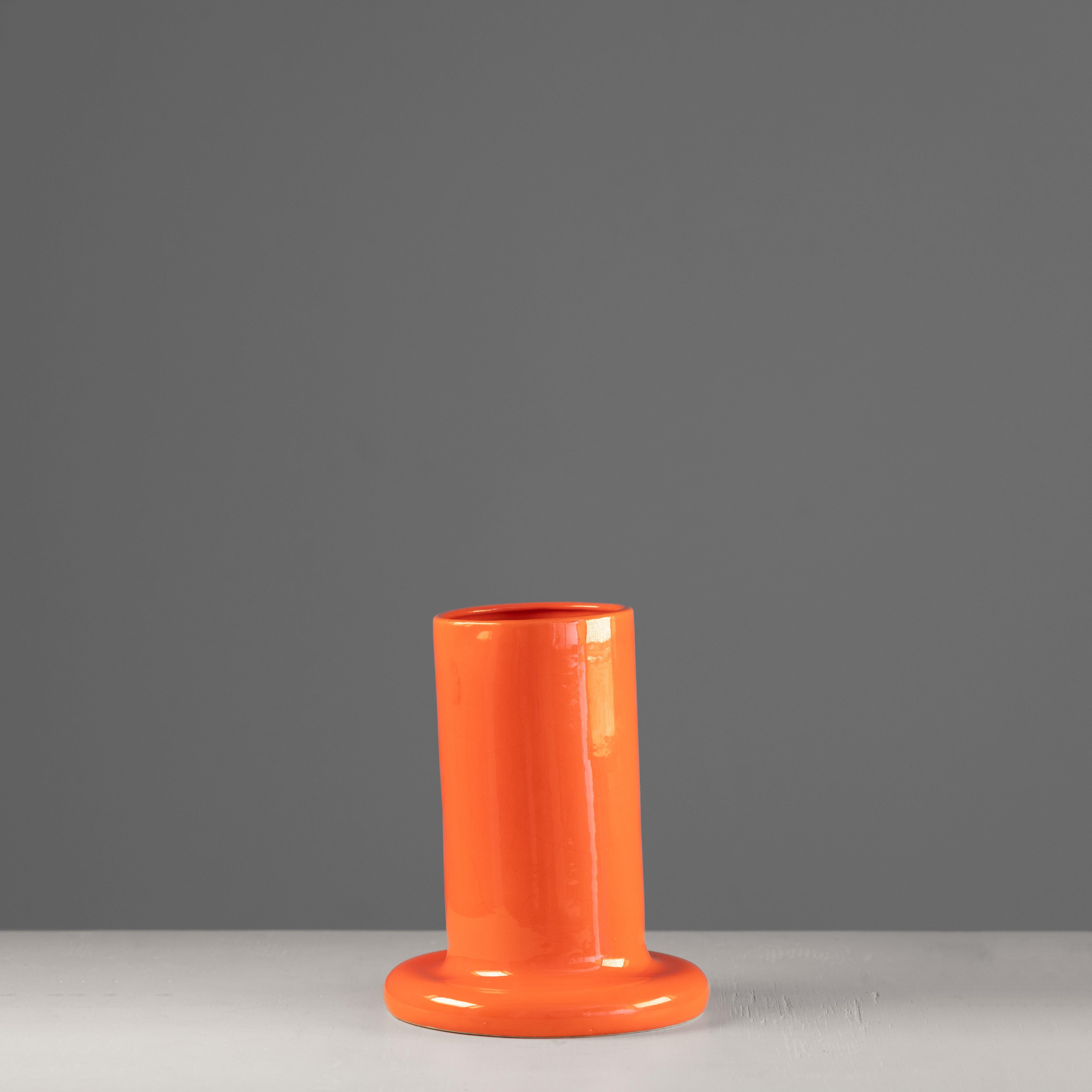 Decorative cylindrical vase with a flared base, made of glazed ceramic in a bright orange color, typical of the Seventies production. The object combines essential lines and chromatic strength, expressing the pop and experimental taste of the time.