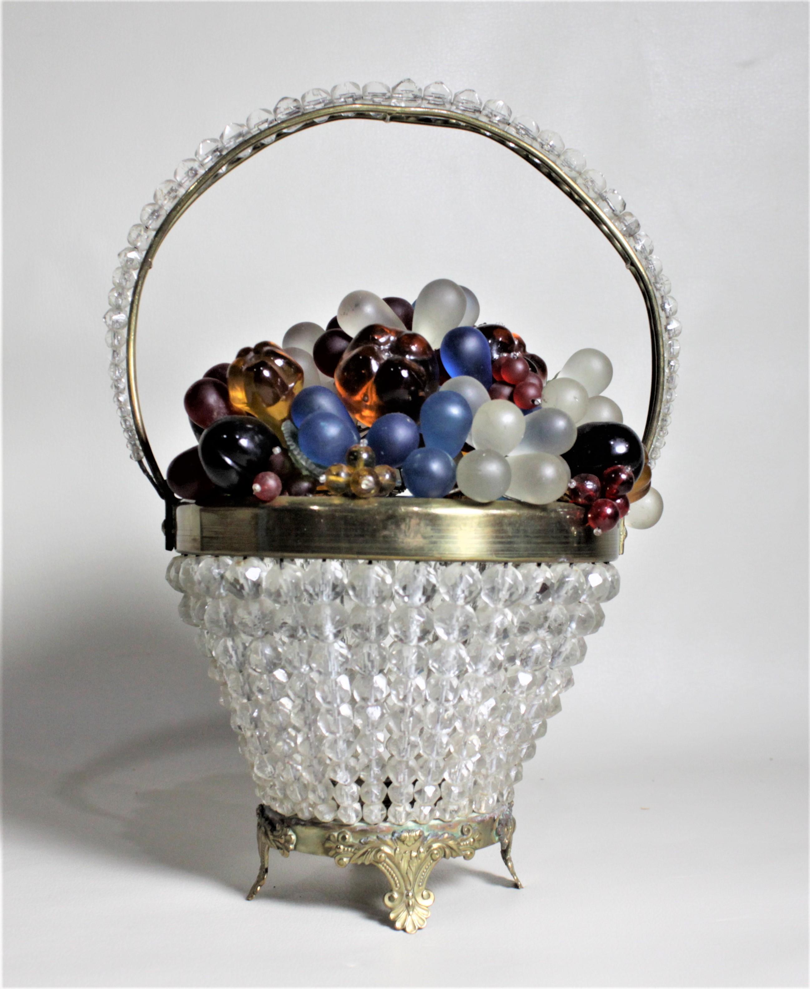 This figural art glass fruit and flower basket was produced in Czechoslovakia in the mid-late 1930s in the period Art Deco style. The base is composed of a series of faceted clear beads making up the exterior of the basket, and accenting handle. The