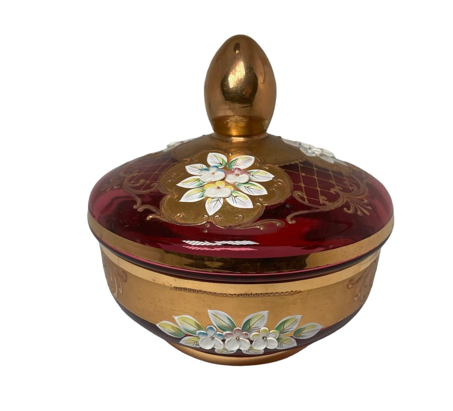 This is a Czech Bohemian Glass Candy Jar. It depicts a light cranberry color lidded Candy Jar decorated with bouquets of hand painted enamel Forget Me Not flowers. Gold and gilt scrolls enhanced the decor of the glass.