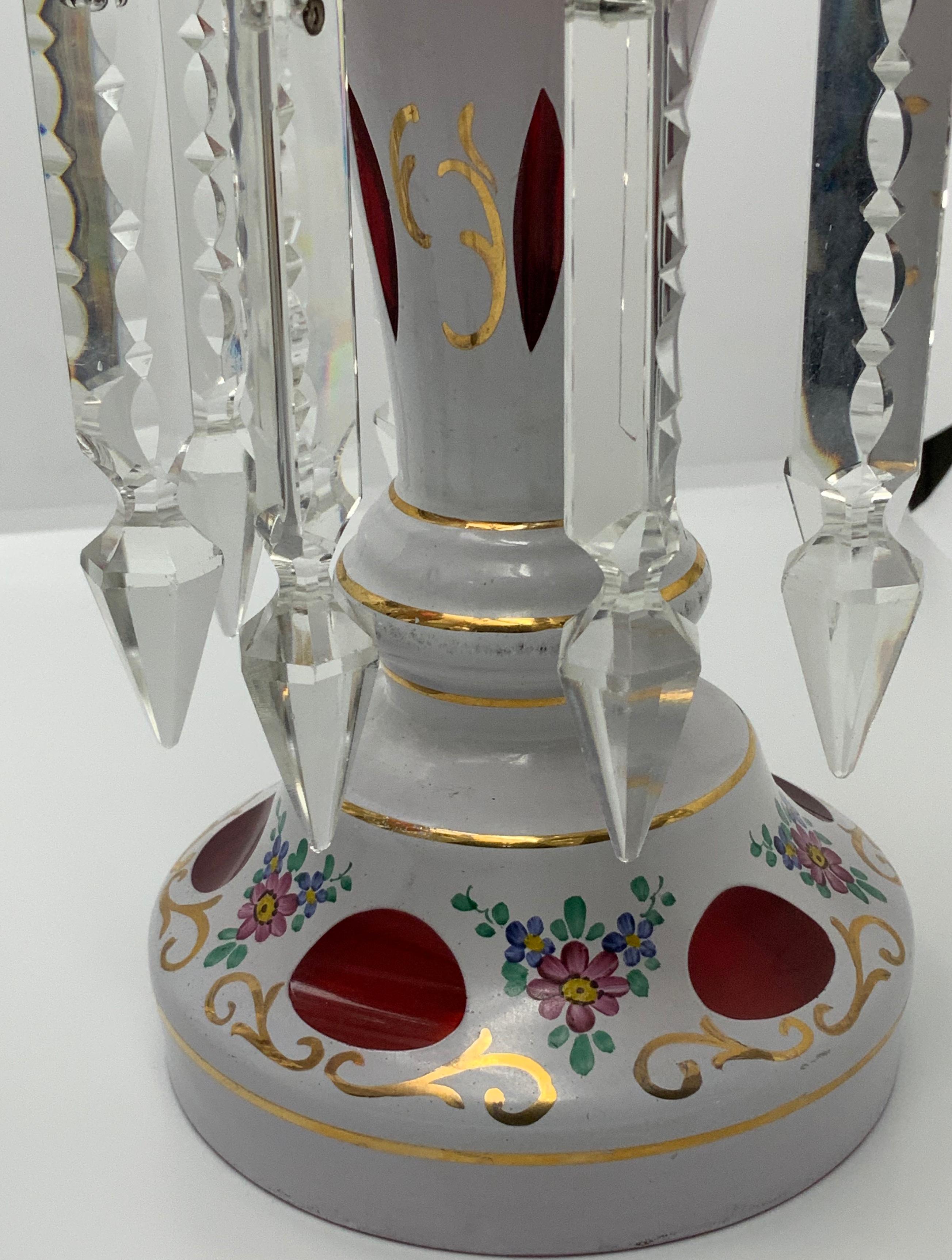 These lusters have a tulip shaped bowl edge that is scalloped and has eight handcut spearhead crystal prism. They are decorated with hand painted flowers, foliage, and gilt scrolls.