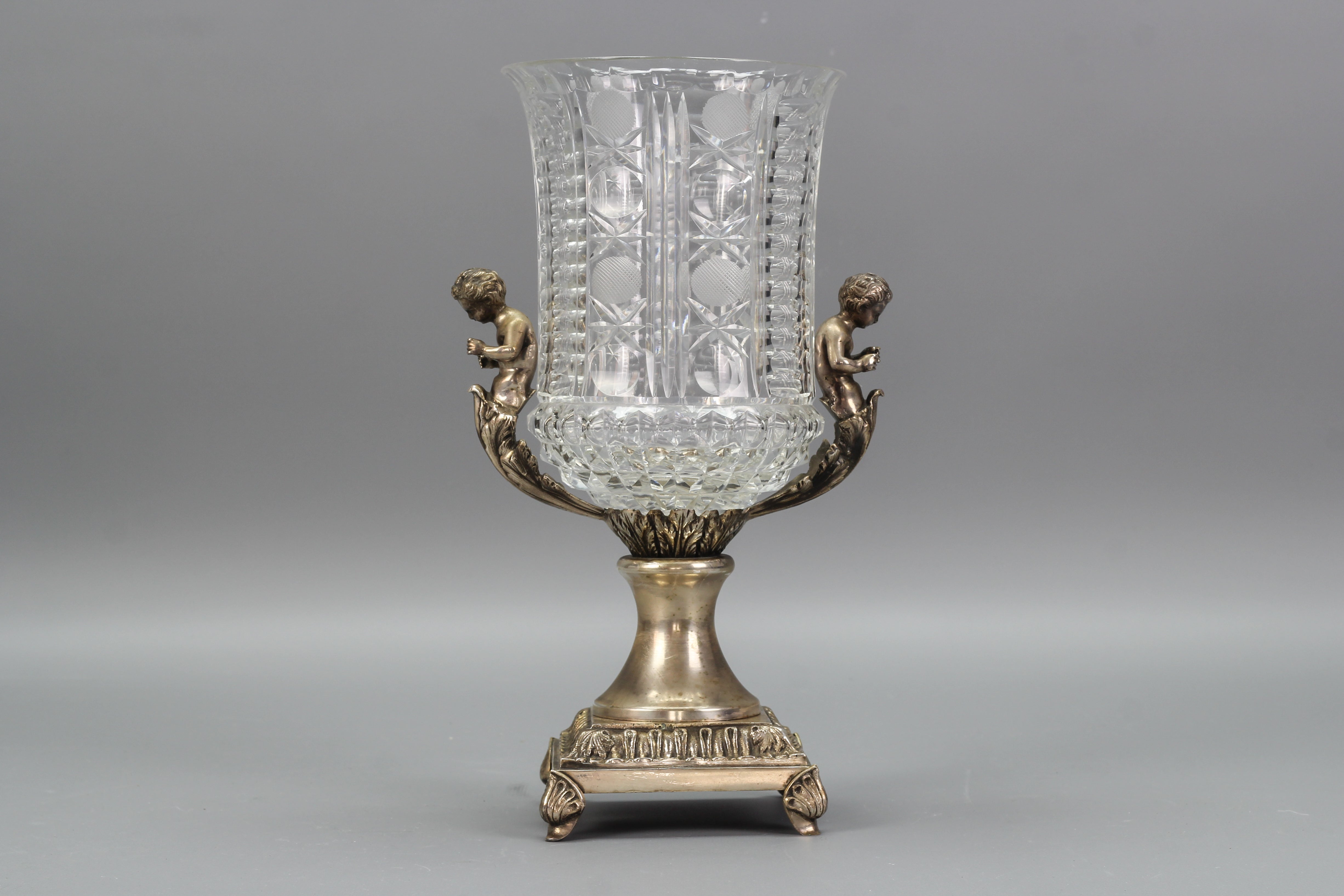 Vase aus tschechischem Kristallglas und Messing mit Putten, ca. 1970er Jahre.
Diese schöne Vase im viktorianischen Stil besteht aus klarem, geschliffenem Kristallglas, das auf Messingfüßen steht und von Putten mit Blattdekor geschmückt