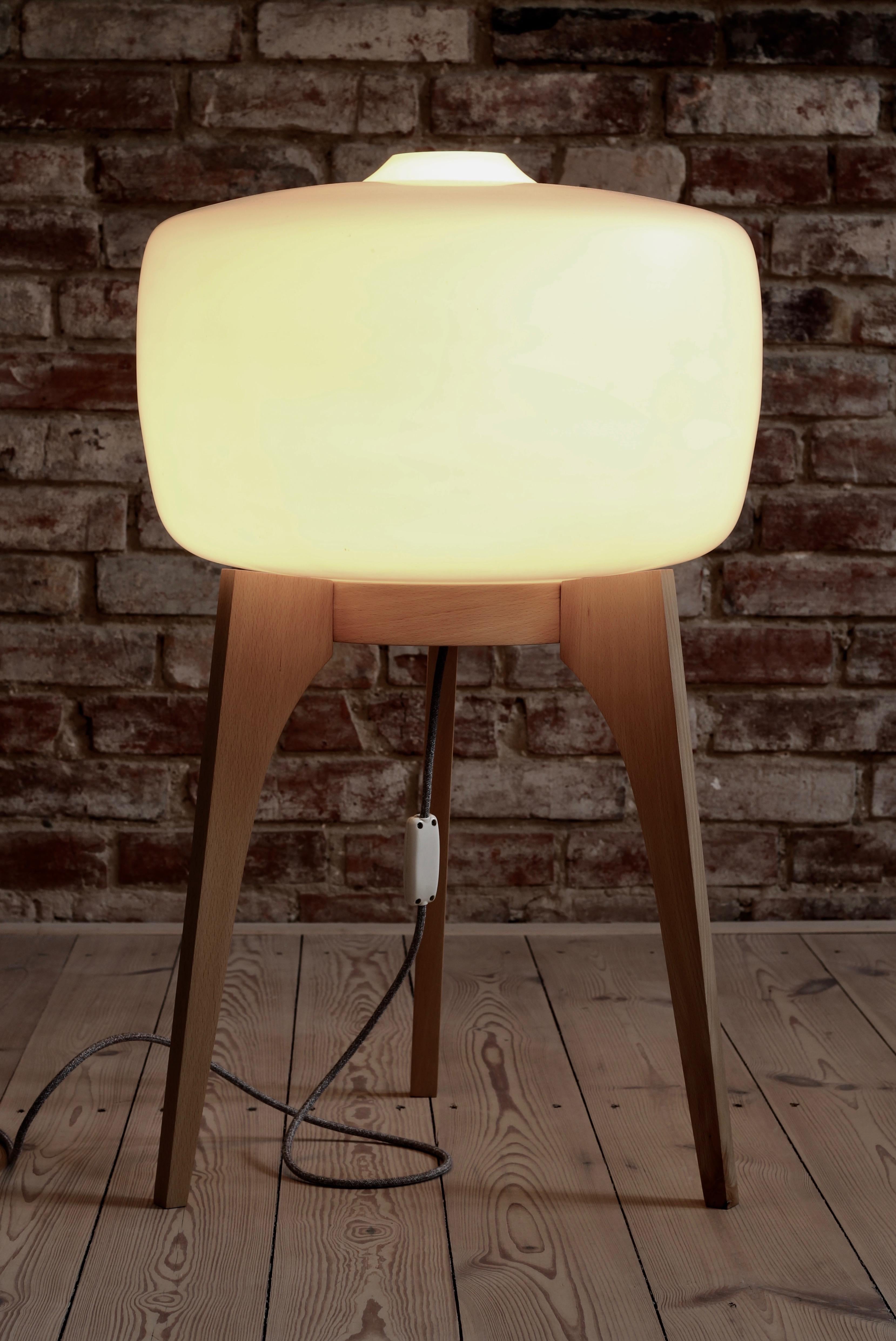 This 1960s floor lamp was made by Czech manufacturer Uluv (Ustredi lidove a umelecke vyroby). It has a large milk-white glass lampshade set on a three wooden legs base. It gives a warm delicate light creating good vibes in the room. The wooden base