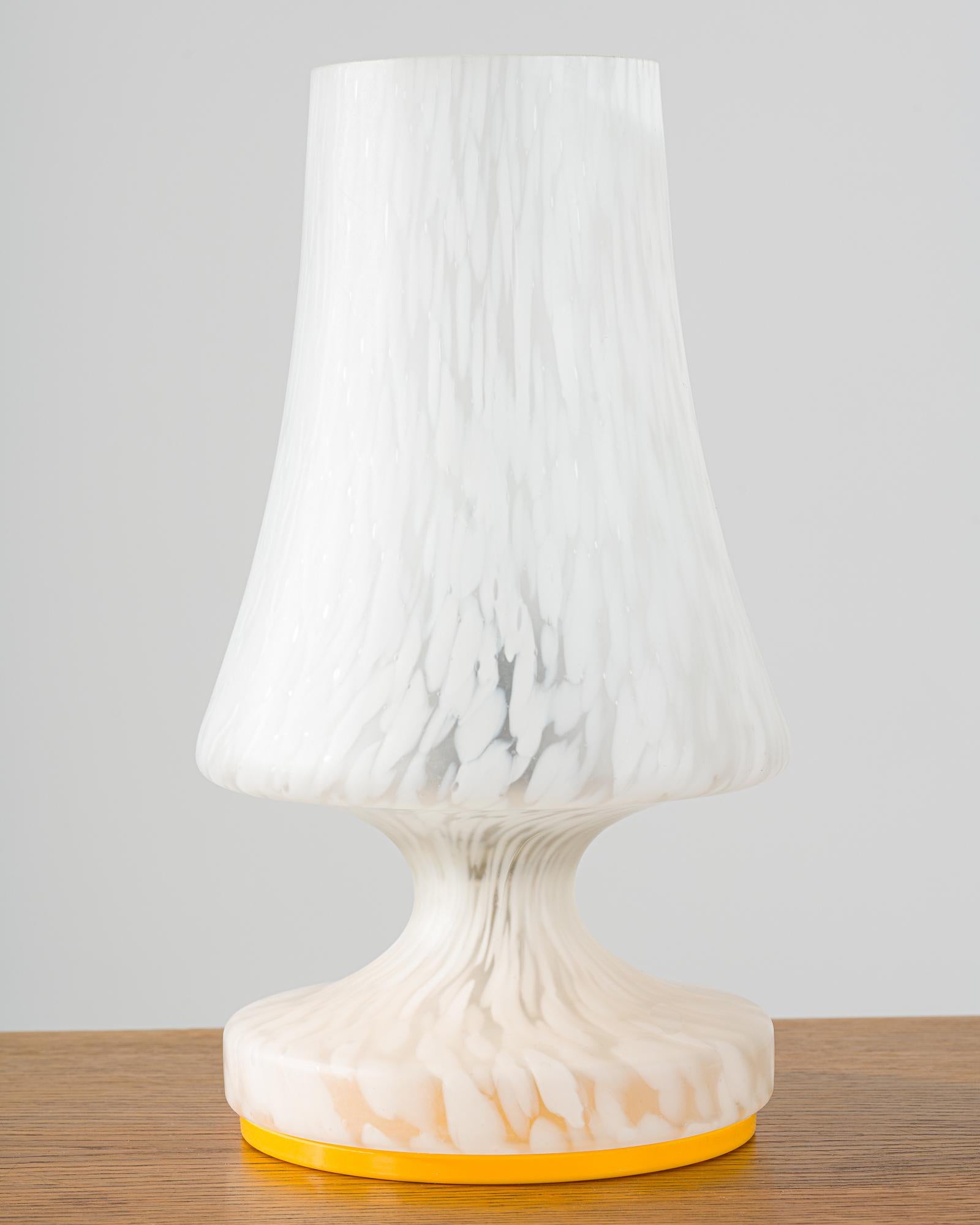 A glass table or bedside lamp produced in Czechia in 1970s. 
The lamp is utmost unique thanks to its white and clear lampshade, as well as the orange base. 
When lit it emits soft light through the clear and white glass shade.
Perfect original