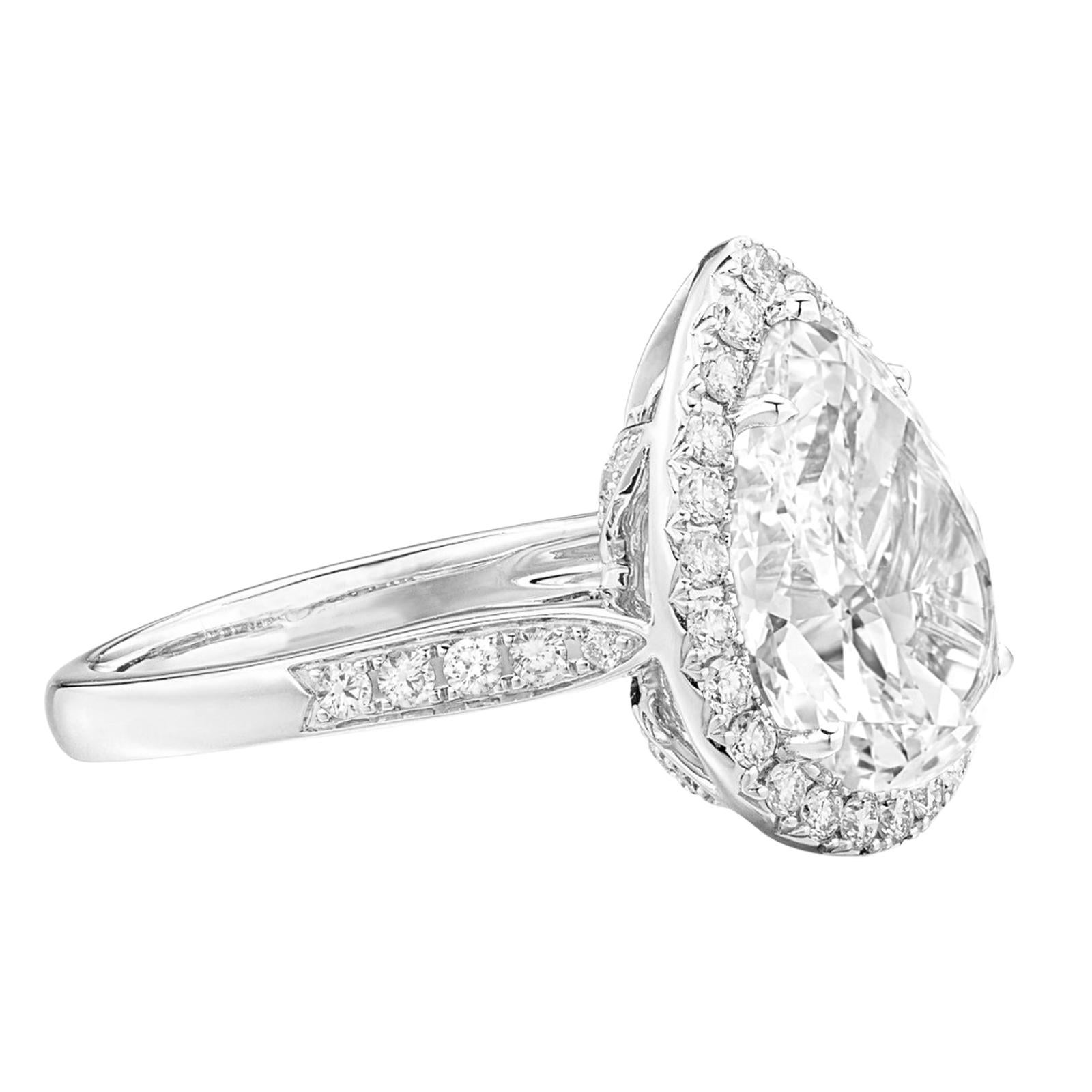 This enchanting ring features a 5.03 carat pear cut diamond, surrounded by a sparkling halo of smaller diamonds and set in luxurious 18K white gold. 

The central diamond boasts a color grade of F, offering a bright and colorless appearance that