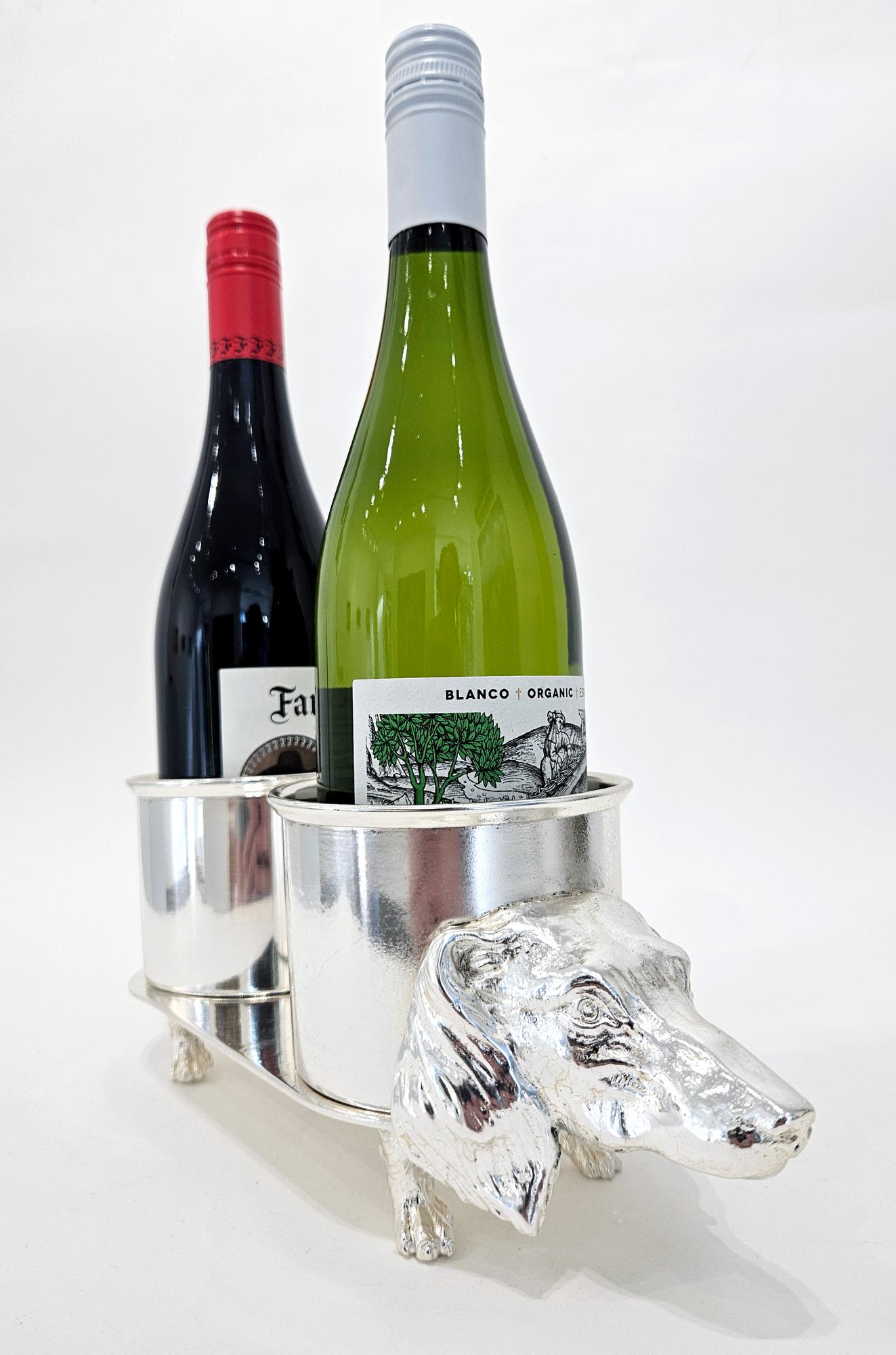 A charming and highly unusual mid century silver plated wine bottle holder in the shape of a Dachshund / teckel or sausage dog. 

Made in Spain in c. 1950, this is a very rare model. In all likelihood it was a private commission. It features two