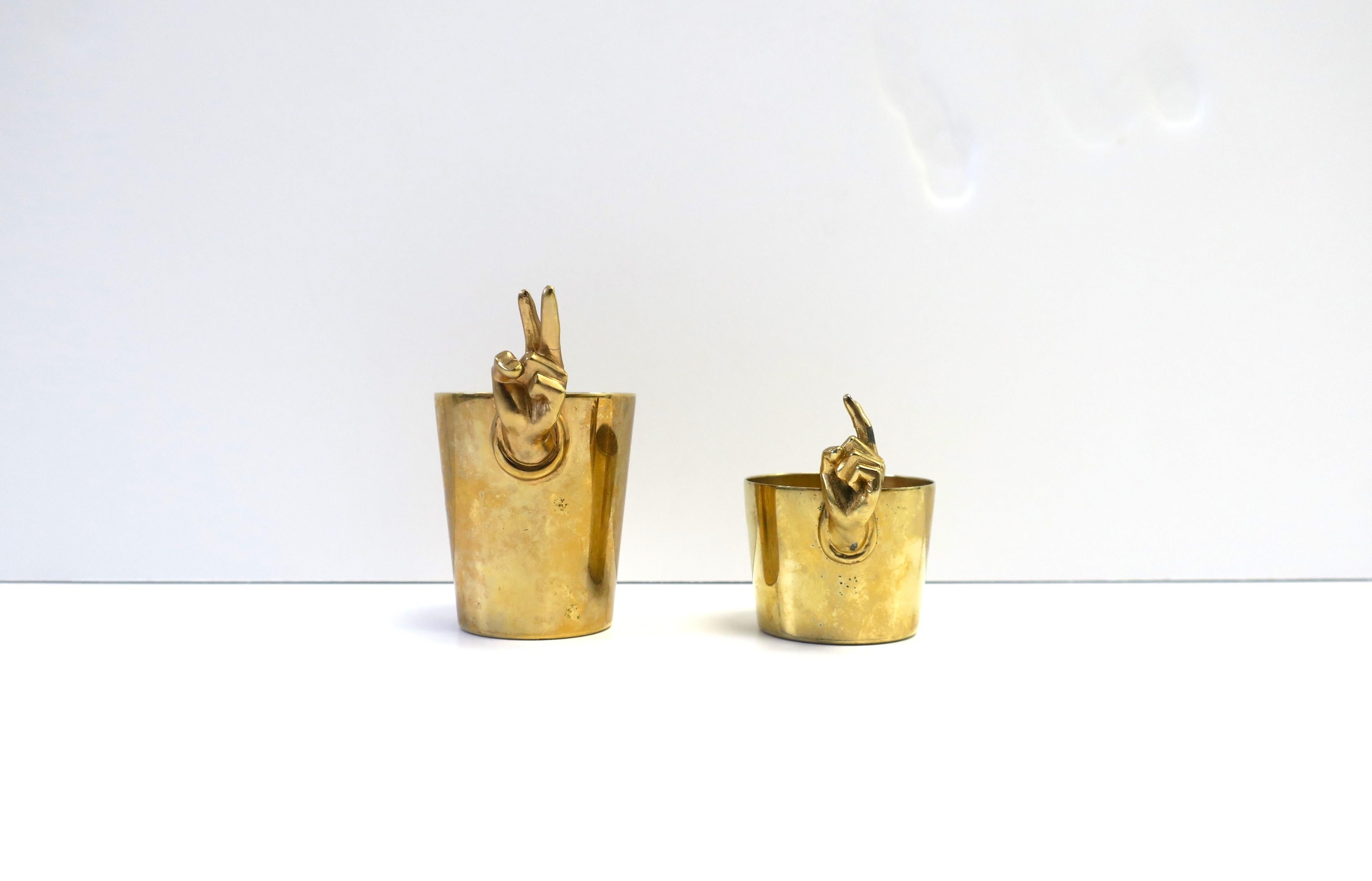 A rare and fun set of two (2) gold plated Surrealism DaDa style jigger shot glasses with hand and finger design by Napier, circa mid-20th century. One hand is in 'peace' sign, the other 'pointing'. Each shot glass has measurement marks for proper