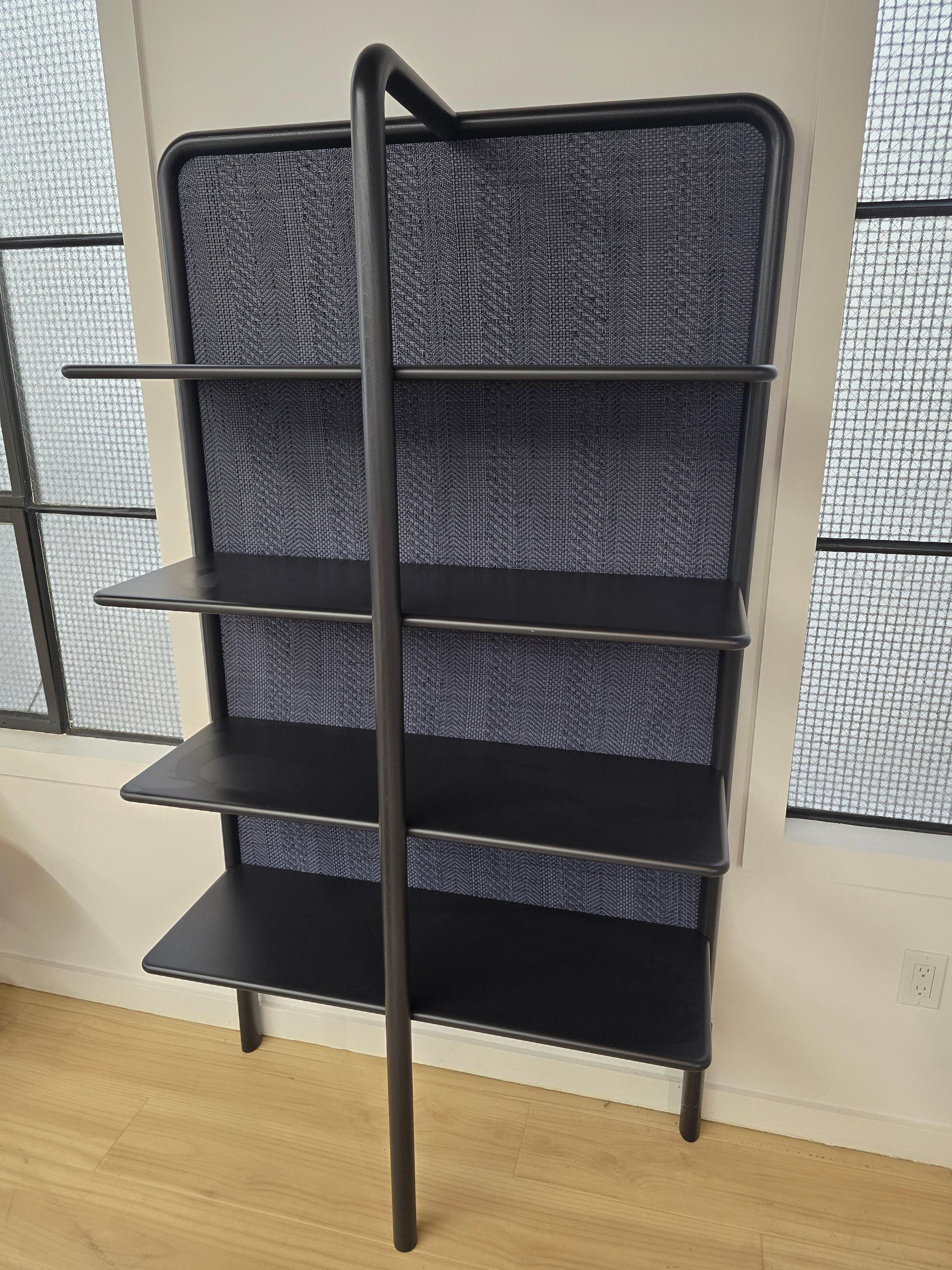 Bookshelf with ash wood frame and MDF shelves lacquered in date, blueberry or ginger colours. Back panel covered in water repellent and cleanable faux-leather vibes in azul. Steel edge profile and spacers for wall mounting, glossy lacquered in