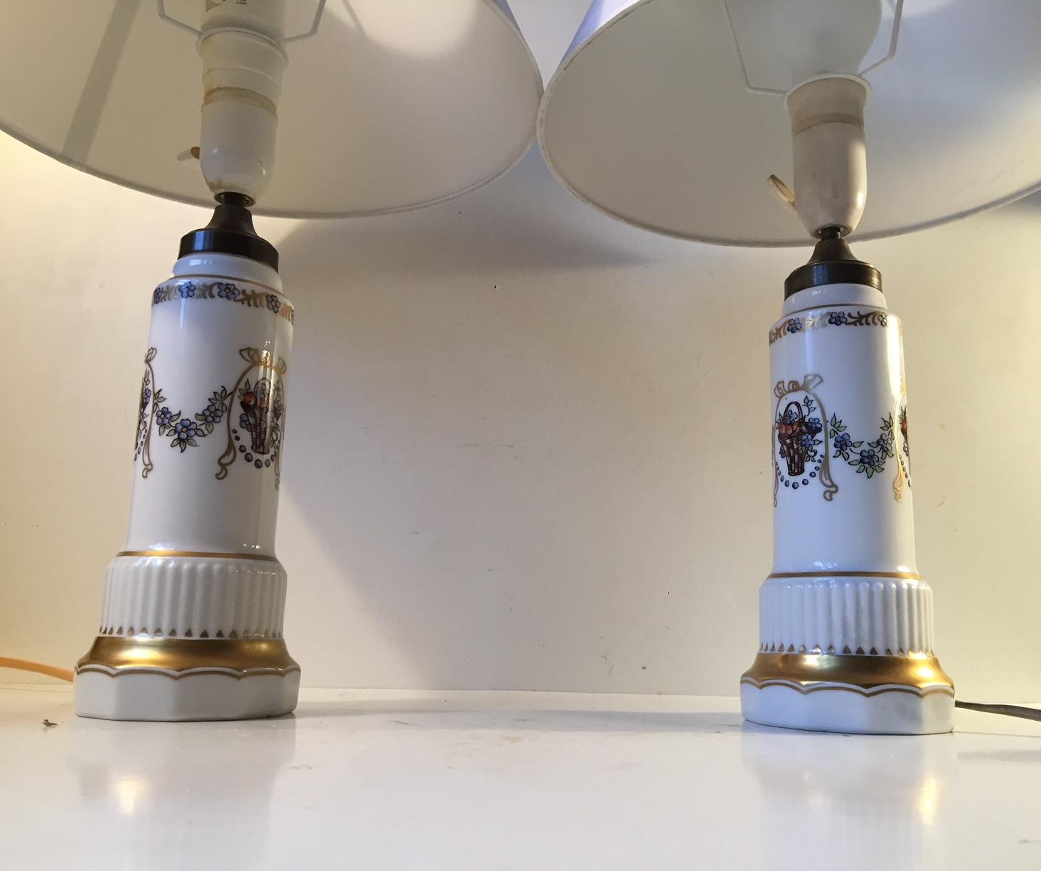 A matching pair of column shaped porcelain table lights by Dahl Jensen. Hand painted with flower- and fruit baskets and partially decorated with gold enamel. Both of them come signed and numbered. The lights come without the white textile shades.