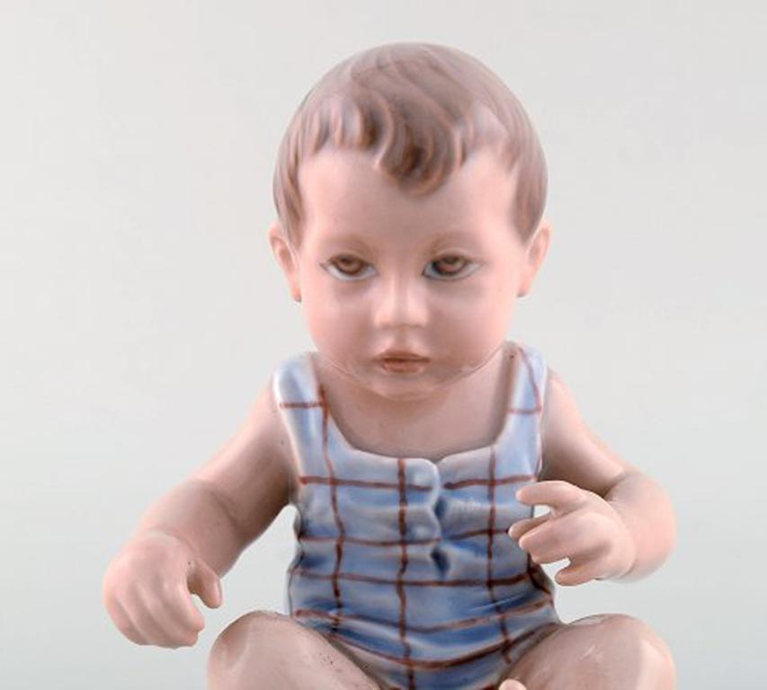 Dahl Jensen porcelain figurine. Baby boy. Model number 1105. 1st factory quality. 1920/30's.
In very good condition. 
Measures: 13 x 11 cm. 
Signed: Kings crown, DJ Copenhagen.