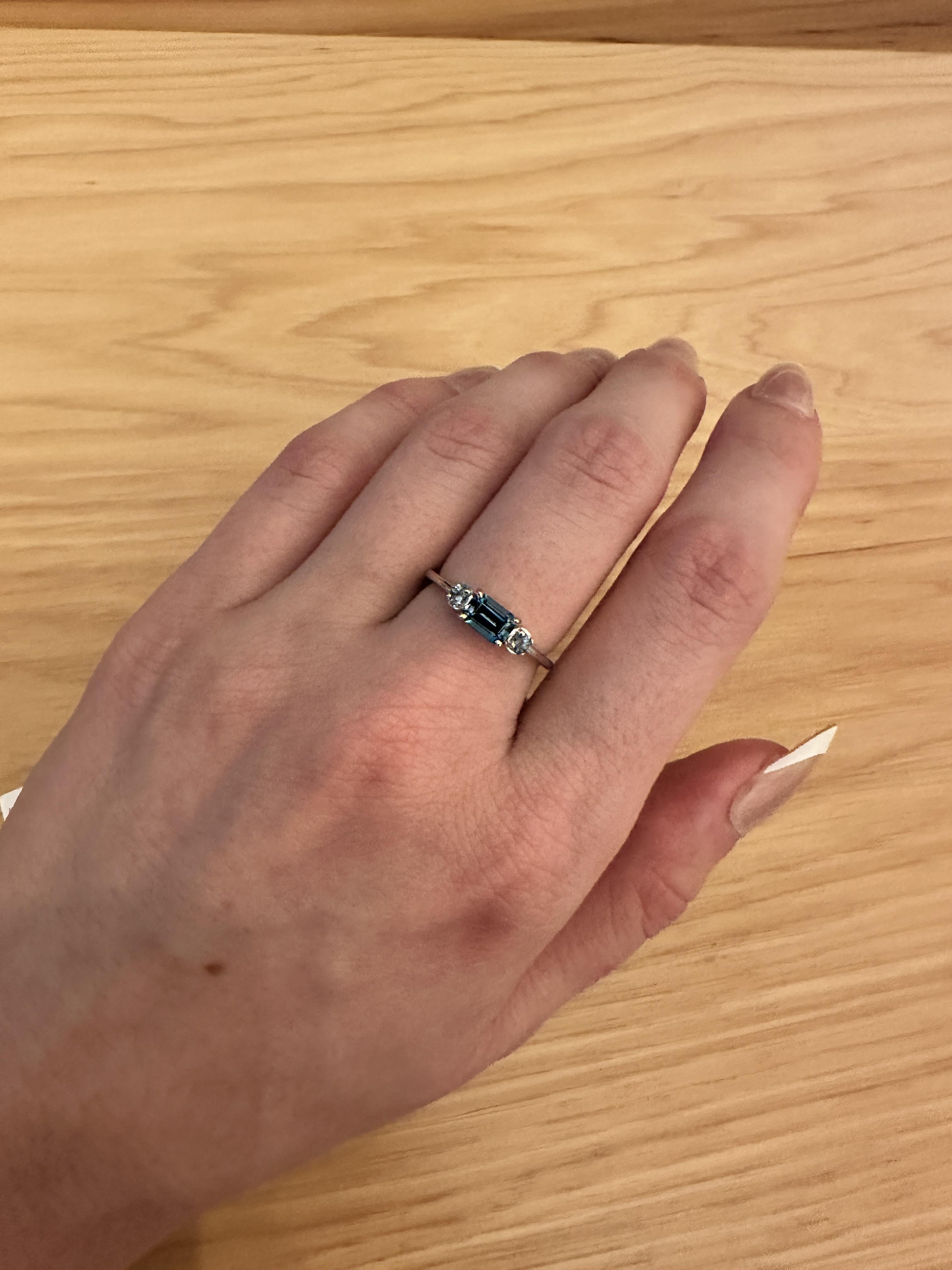 Este precioso anillo de este a oeste presenta un Topacio Azul de Londres de talla esmeralda con acentos de diamantes azules. Un delicado diseño de anillo perfecto para un compromiso o aniversario llamativo. Este anillo también es un bonito regalo de