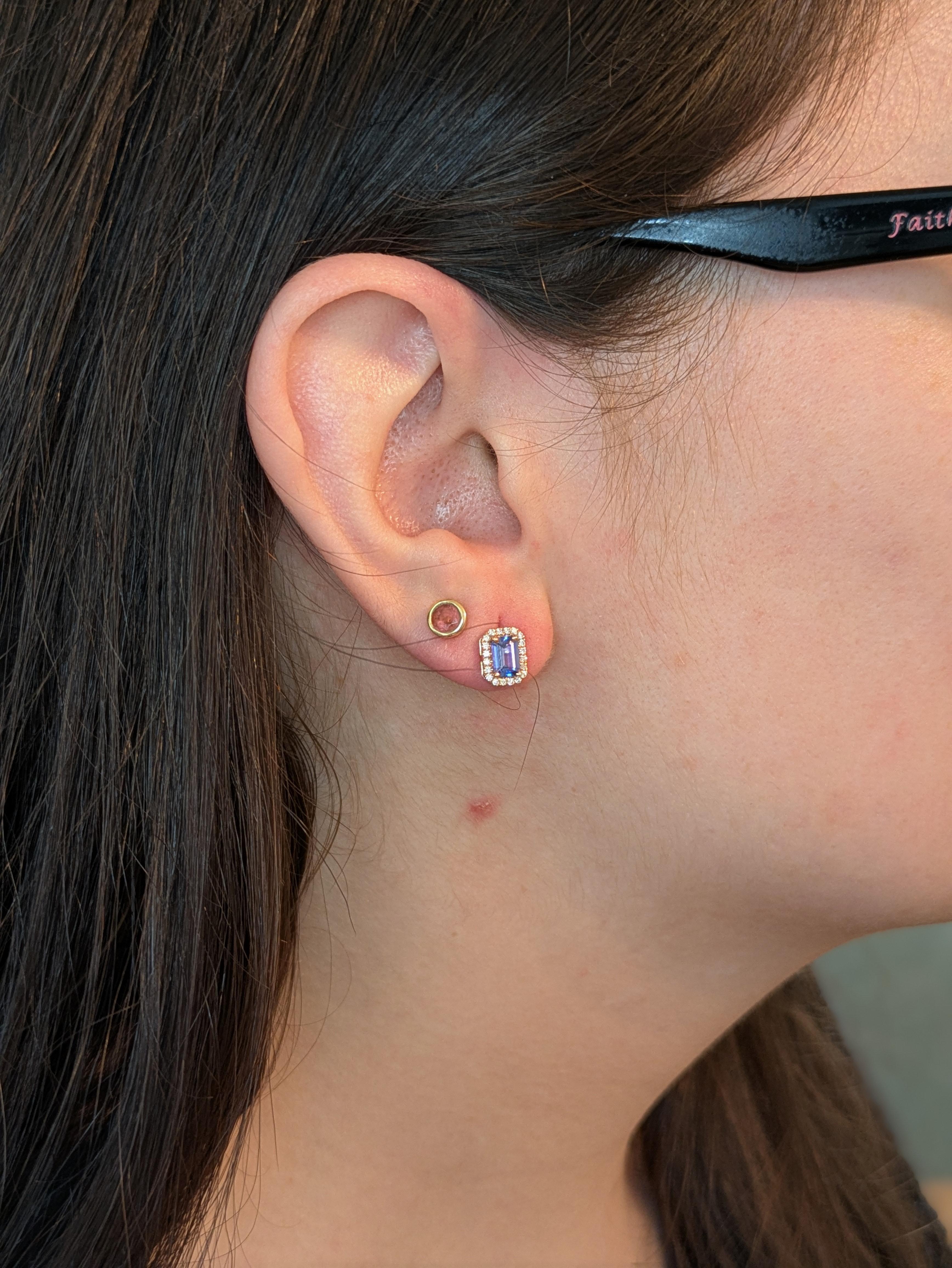 These dainty emerald-cut tanzanite stud earrings exude elegance with their mesmerizing violet-blue hue. Each tanzanite is encircled by a sparkling halo of earth-mined diamonds, enhancing their brilliance. Set in 14K real rose gold, These earrings