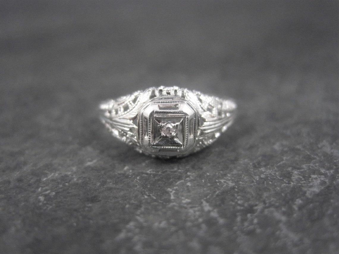 This gorgeous antique diamond ring is 10K white gold.
It would make the perfect promise ring or engagement ring for that girl that likes the minimalist look.

The diamond is a tiny, 1.5mm stone.

The face of this ring measures 5/16ths of an inch