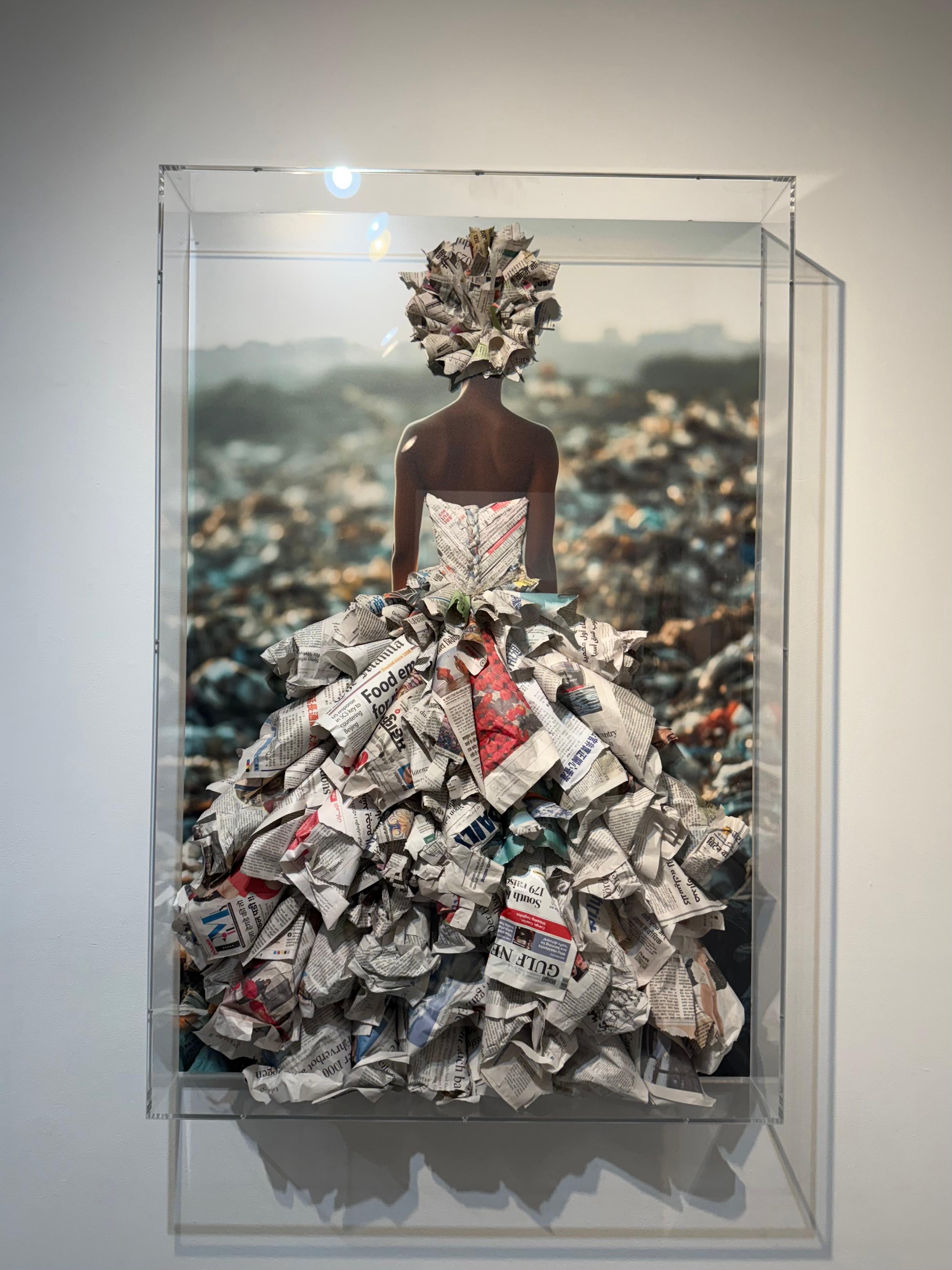 Garbage Queen is a striking mixed-media series that blends photography with physical waste — discarded plastics, newspapers, and other salvaged debris — assembled into sculptural garments and affixed to the surface of each print. The images are