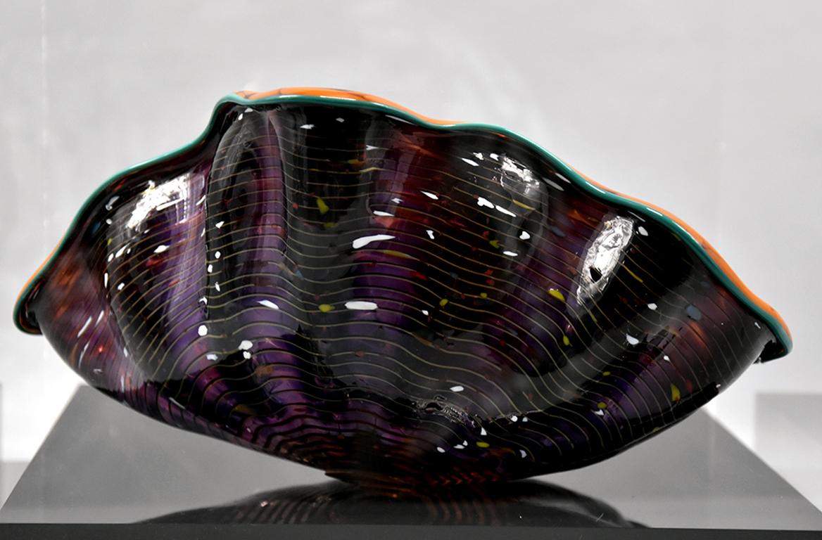 Dale Chihuly is inspired by the organic forms of the sea and ever changing colors visible in the translucent purple of the outer layers speckled with opaque white, yellow, greens, orange, and blues that enliven the surface. The interior orange forms