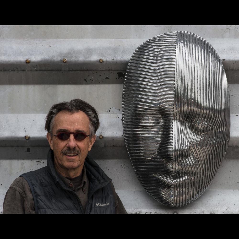 A large, striped mask in polished aluminum is set in a peaceful quiet expression by Dale Dunning. This wall sculpture is the artist's proof from an edition of 9.
