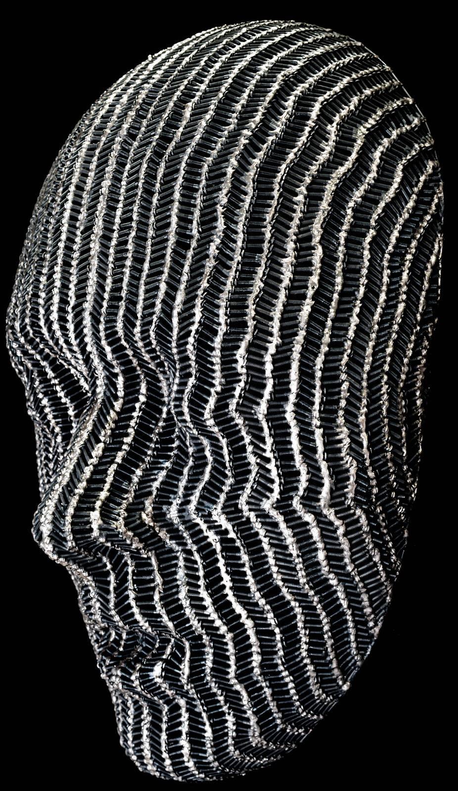 Hundreds of machine screws and bronze are skillfully shaped to create the folds and curves of a large mask. The silent face, its eyes closed, exudes a darkly romantic sensibility that recalls the mystery and aura of Gothic literature. This sculpture
