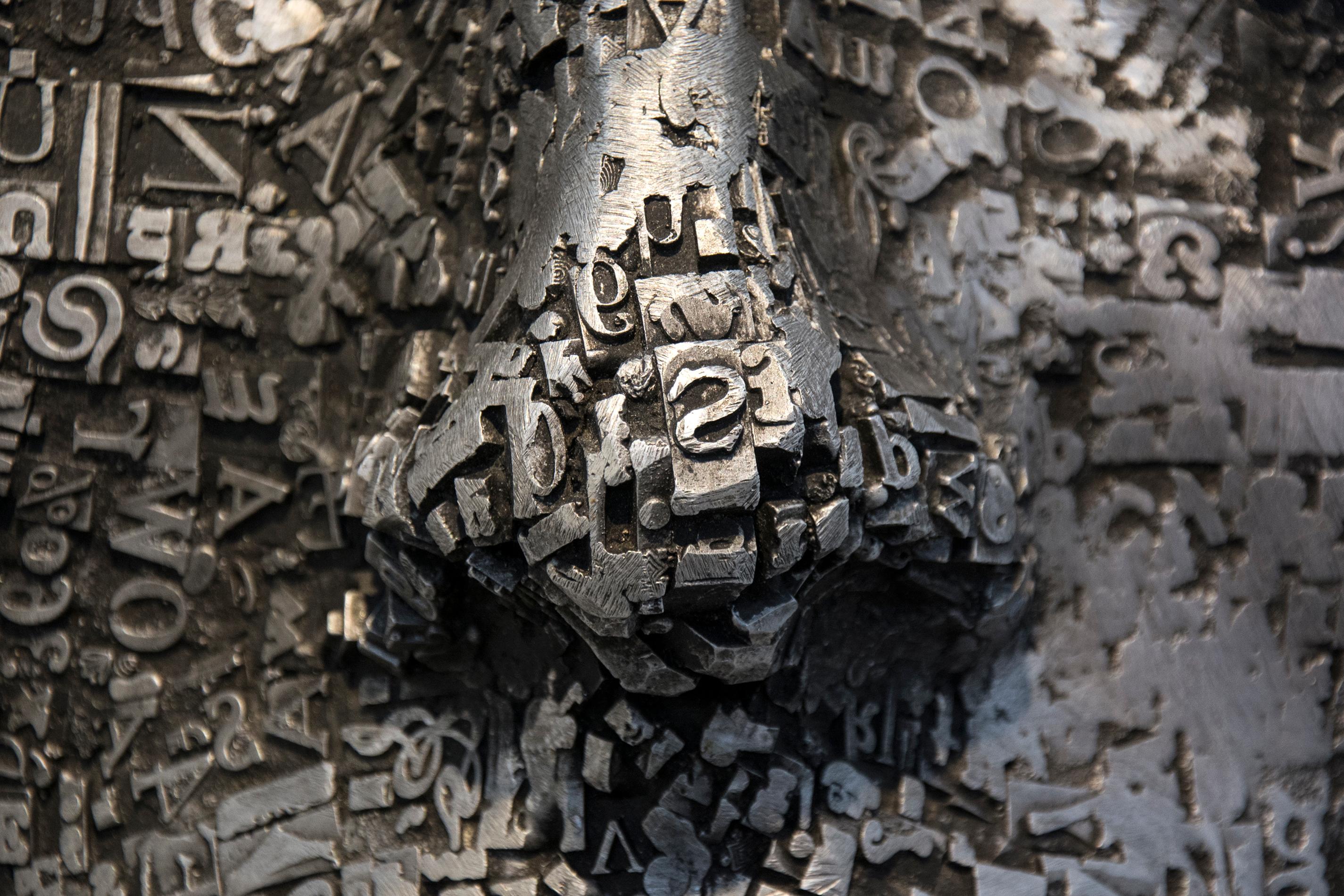 Repurposed metal type was fused in the shape of a mask then cast in aluminum and polished to create a rich surface by artist Dale Dunning. The title of the work palimpsest refers to a surface on which original writing has been erased to make way for