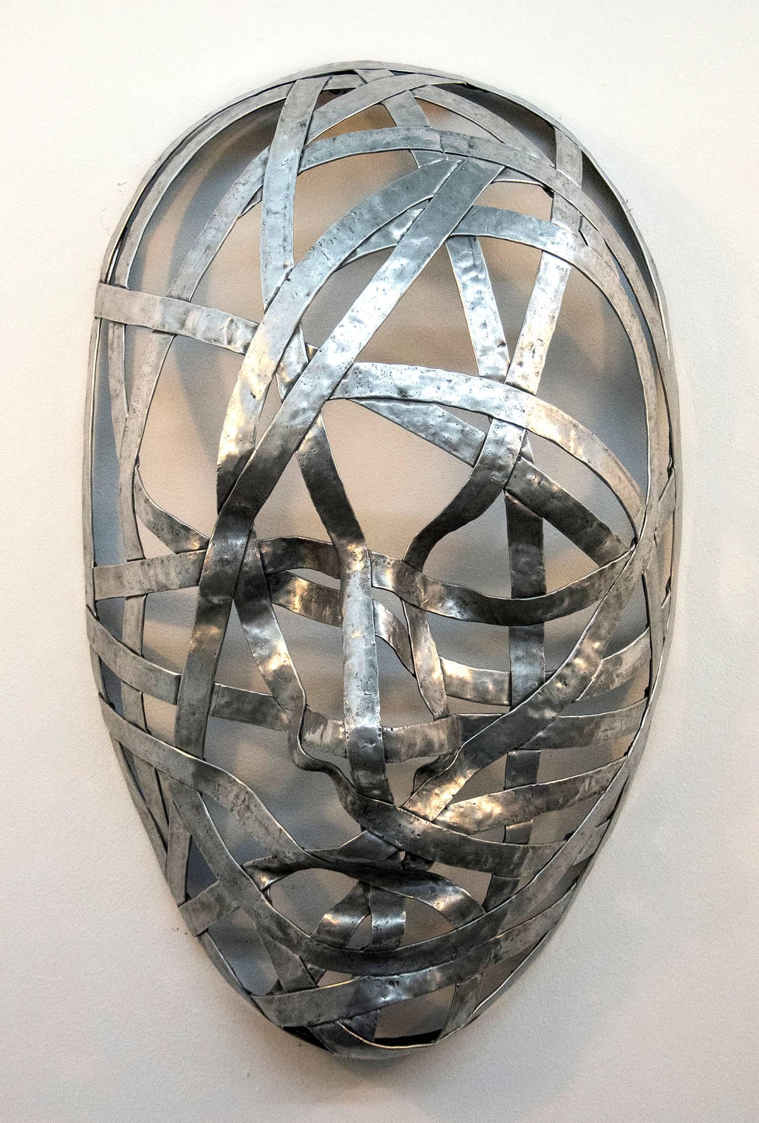 Narrow strips of aluminum are skillfully shaped into the curves and folds of three masks by sculptor Dale Dunning. The industrial steam-punk inspired wrapped faces that change from right to left also reflect a romantic sensibility recalling the