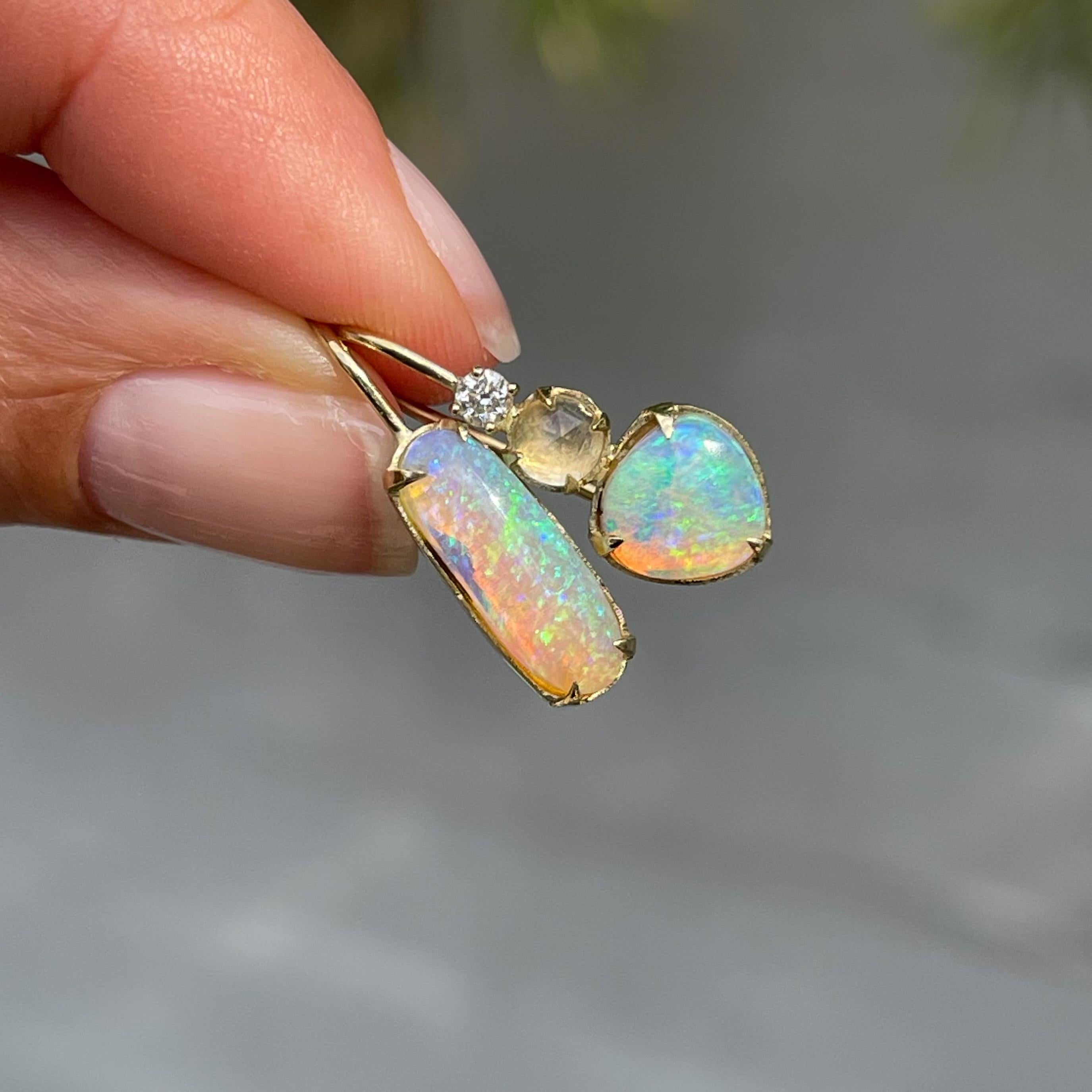 The Dalliance Crystal Pipe Opal Drop Earrings marry crystal opal and blue moonstone in a mystical affair.  Two green crystal opals flicker with intensity, while shades of pink and purple glow through their forms.  On the left, a single oval opal
