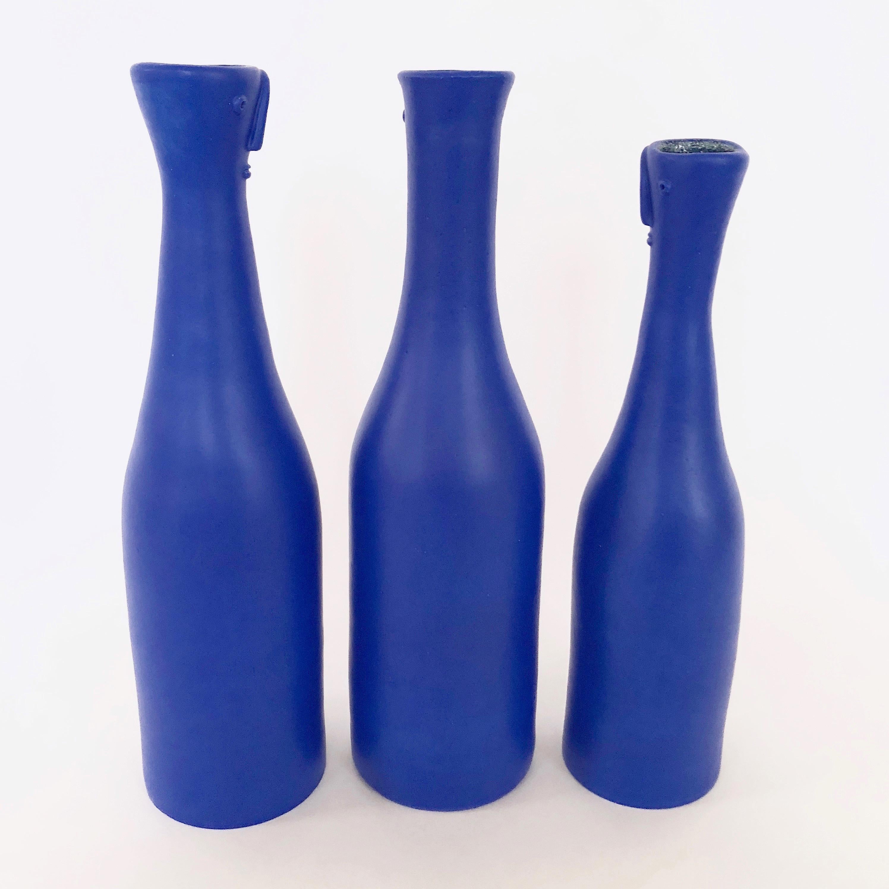 Set of ceramic bottles, figurative shaped, ceramic glazed in deep blue, decorated with stylized faces sculpted front.
One of a kind handmade pieces, signed by the French ceramicists, the Dalo.

The dimensions approx are: 
Bottle 1: H 38.5 cm - D 10