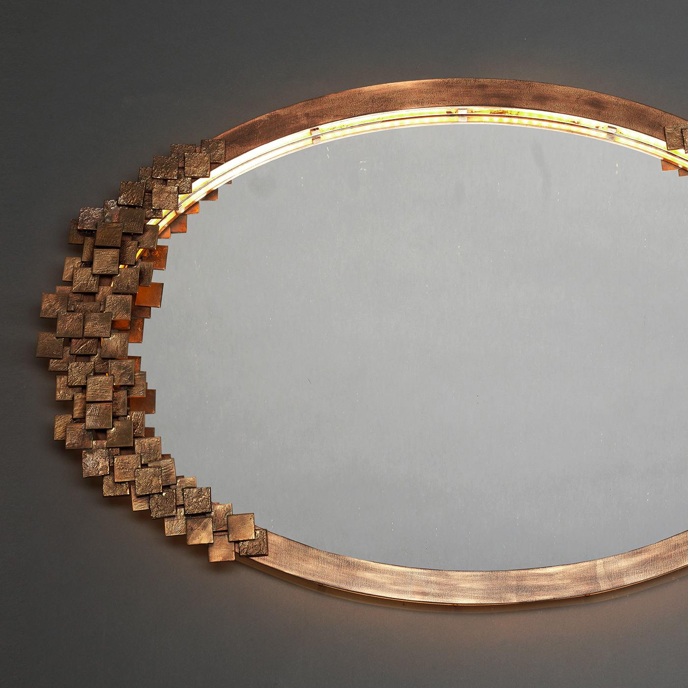 This unique mirror is an elegant choice for both classic and contemporary interiors. The oval brass shape is adorned on both ends with a series of small bronze tiles that create striking reflections, thanks to the LED strip that follows the