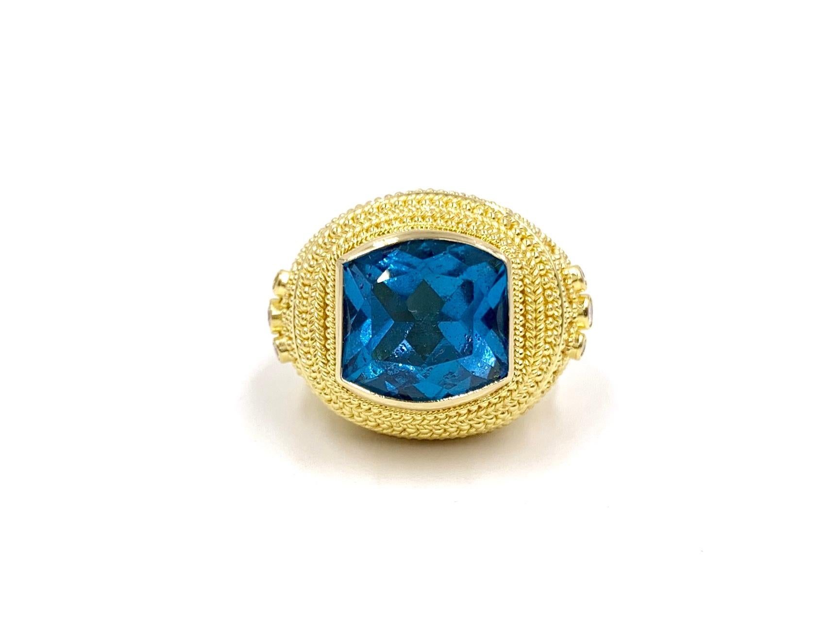 Crafted by expert goldsmith company, Damaskos in Athens, Greece. This beautiful 18 karat yellow gold hand made ring features a large cushion cut London blue topaz center with three round diamonds on each side. Diamond total weight is approximately