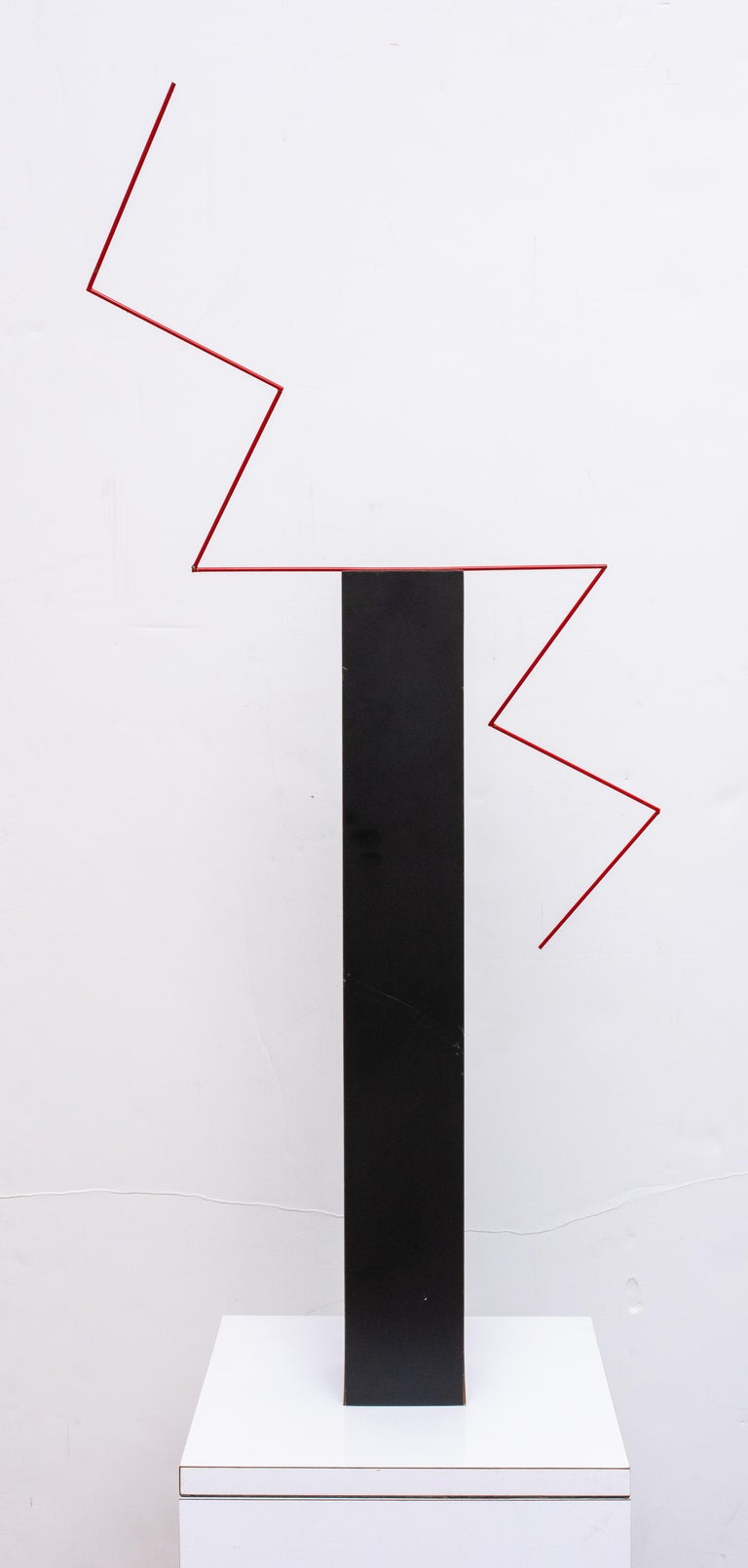 Postmodern abstract sculpture, the black-veneered square shaft surmounted by a red-enameled metal lightning bolt, above a white-veneered base on conforming white-veneered pedestal.

Measures: 38