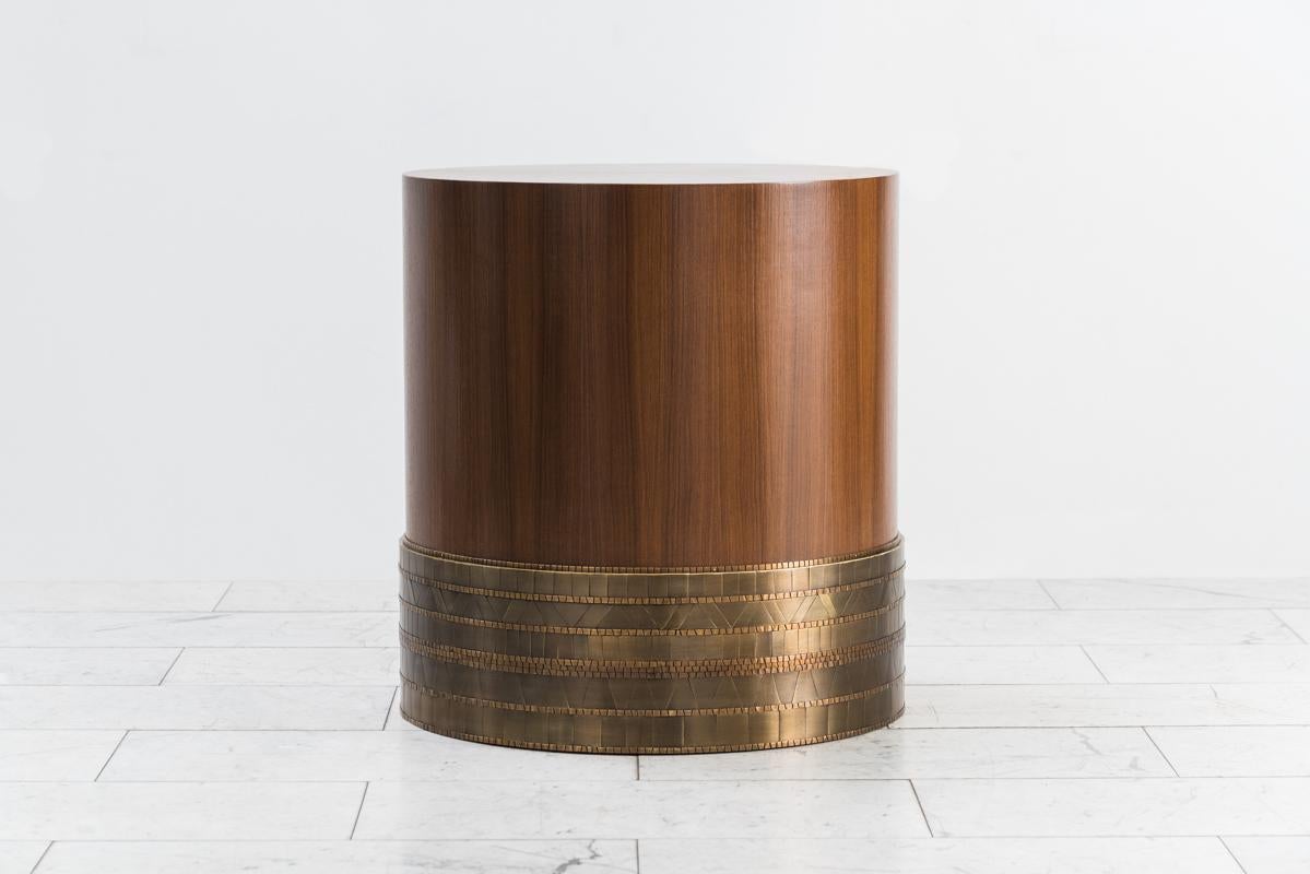 Damian Jones’s Rhoss table functions perfectly as a side table or cocktail table. Its drum shaped form is sheathed in a mosaic pattern of hand-cut and laid brass “tiles.” Each tile has been patinated in varied colors and shades creating facets that