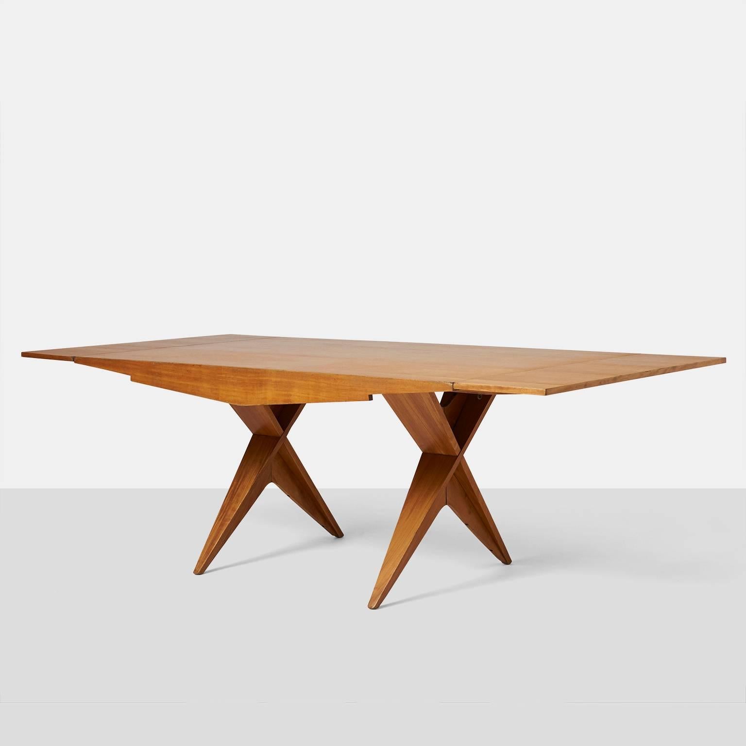 A drop-leaf dining table in blonde mahogany on architectural X-base legs by Californian designer Dan Johnson. With the leaves extended the table measures 90