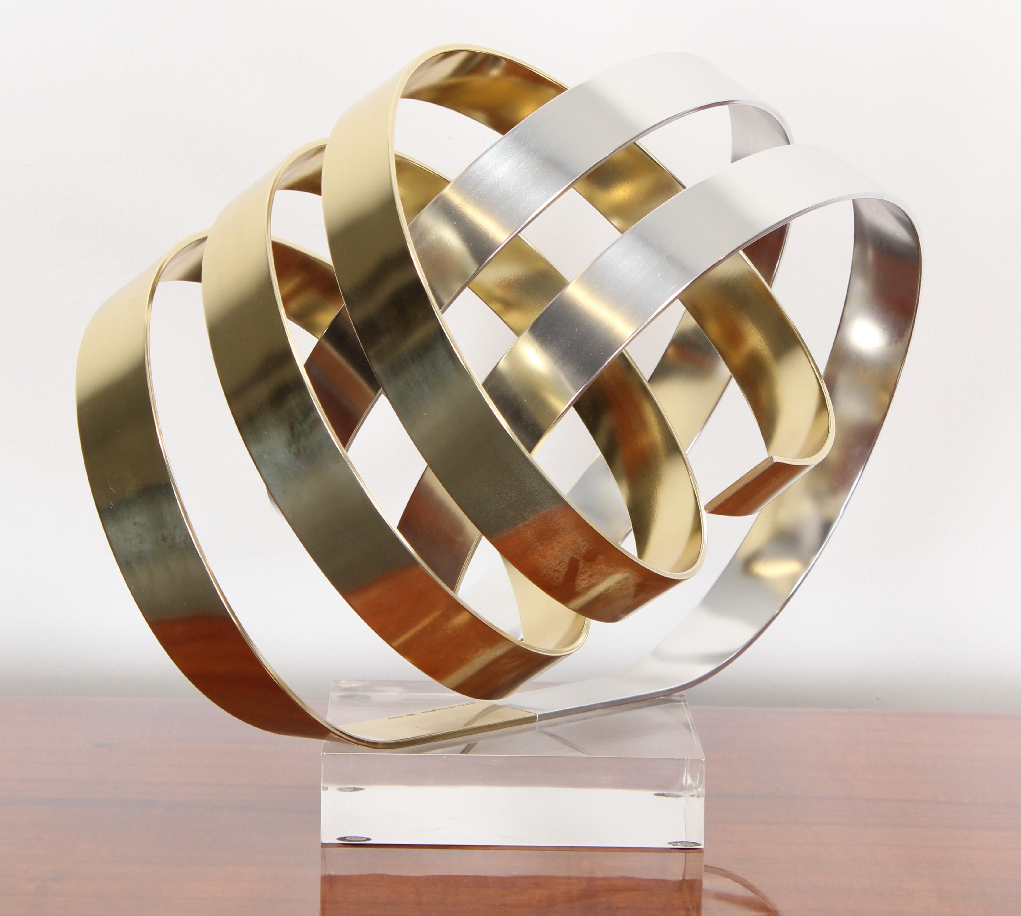 A Dan Murphy ribbon sculpture made of gold and silver aluminum on an acrylic base. Signed and dated 1983.

Dimensions: 13.25