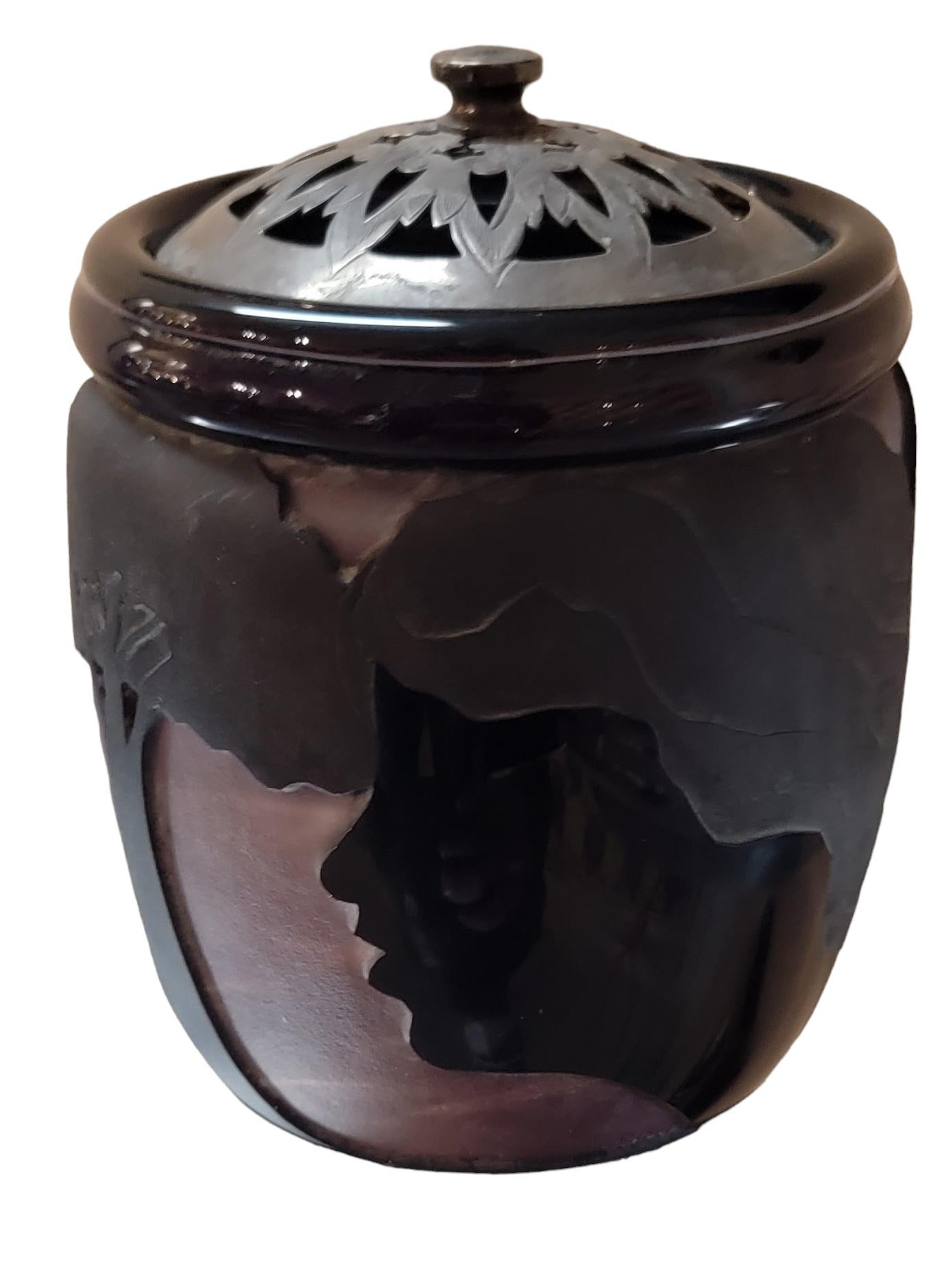 Decorative Vase By Dan Shura with silver lid. The silvered lid has very small cu outs for circulation of air trough the jar. The jars cylindrical design has images of a tree and on the sides of the tree being separated is a man and a woman. Giving