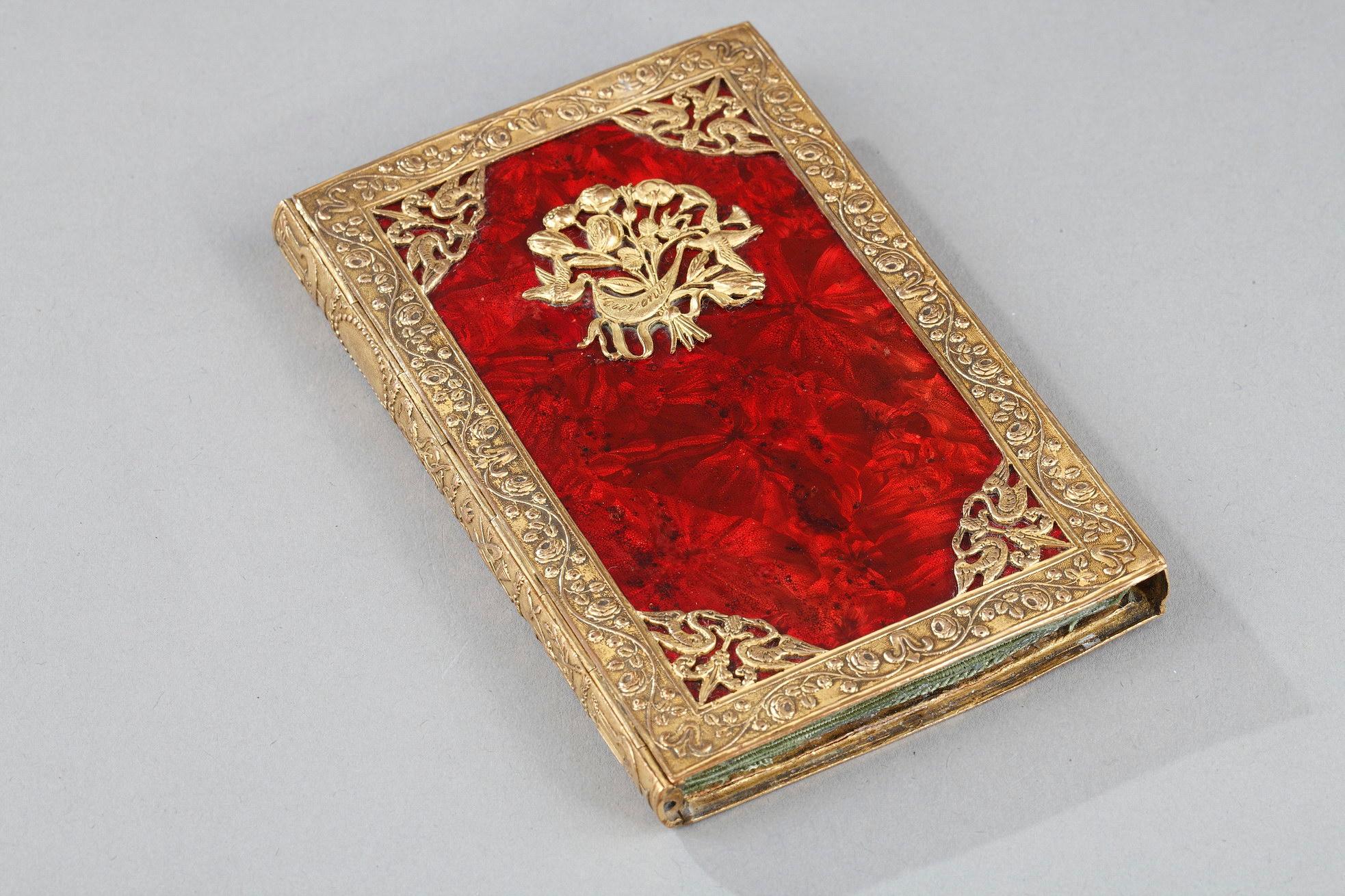 Rectangular dance case in gilded bronze and red colored metal with moire reflections. The gilded bronze mount is finely chiseled with floral friezes, doves patterns in the corners. On the main face, two doves carry in their beaks a motto 
