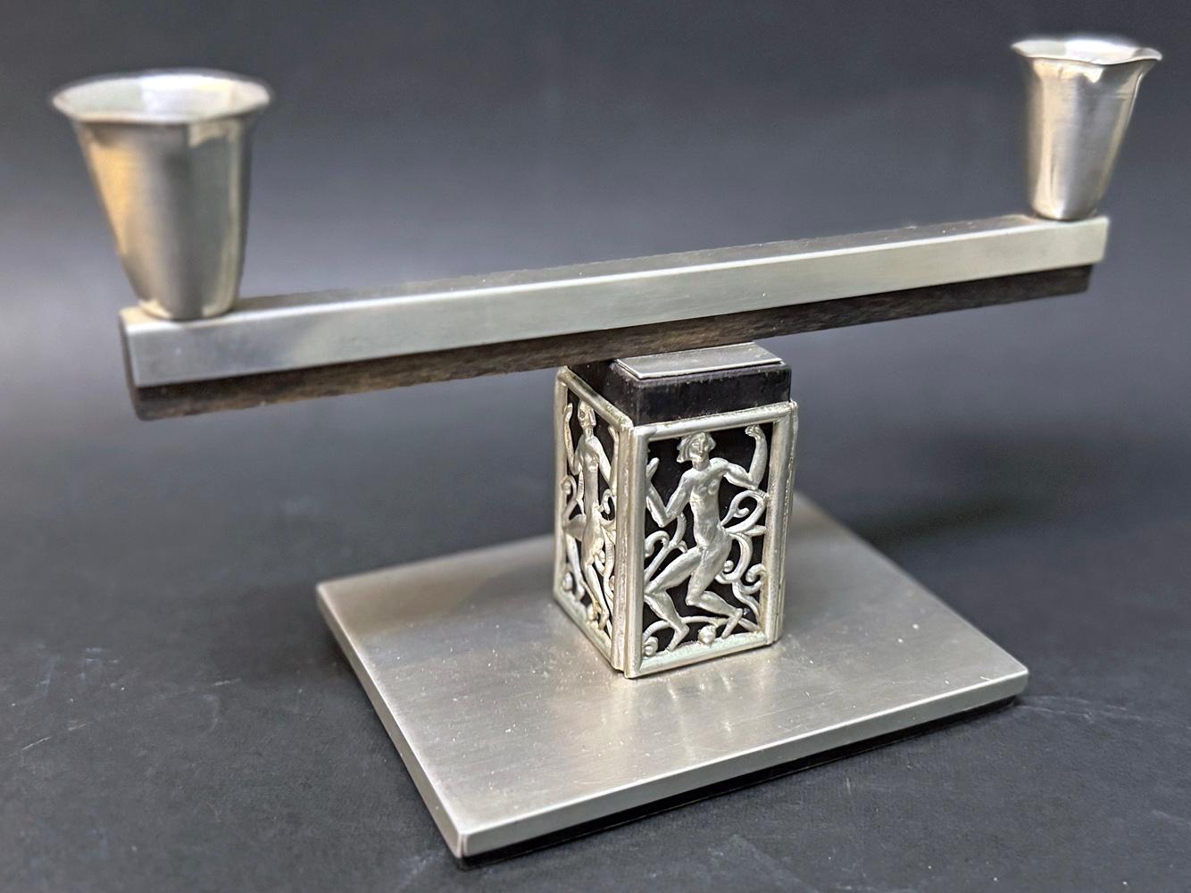 Questo candelabro a due bracci in peltro è sostenuto da una base con una figura femminile nuda e danzante su tutti e quattro i lati.  La simmetria e le linee del candelabro incarnano magnificamente l'eleganza e la raffinatezza dello stile Art Déco