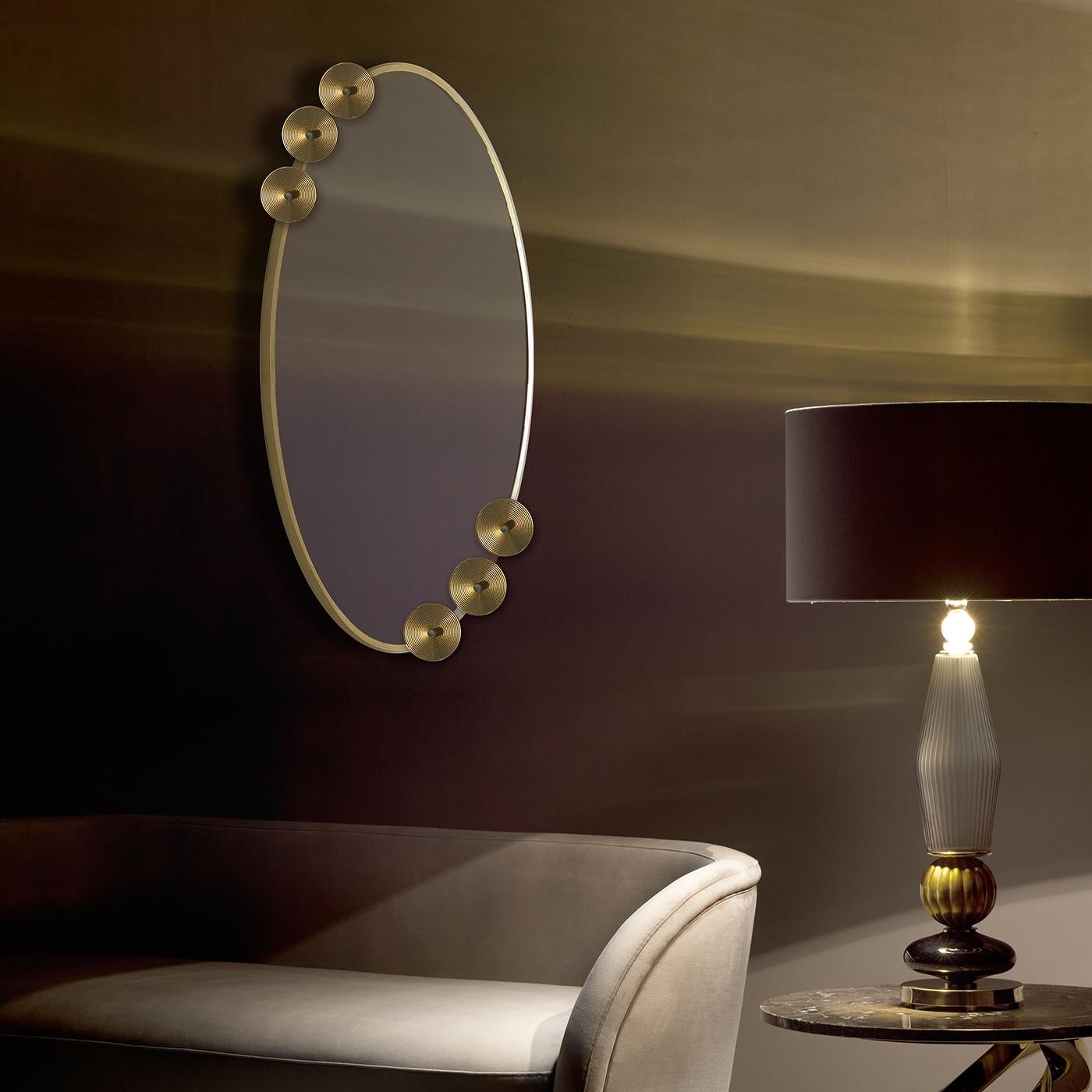 A superb example of artistic craftsmanship, this exquisite mirror is an eye-catching decoration for the wall. Its oval glass frame with an antique gold finish is adorned with two sets of three disks that add a unique embellishment to this piece and