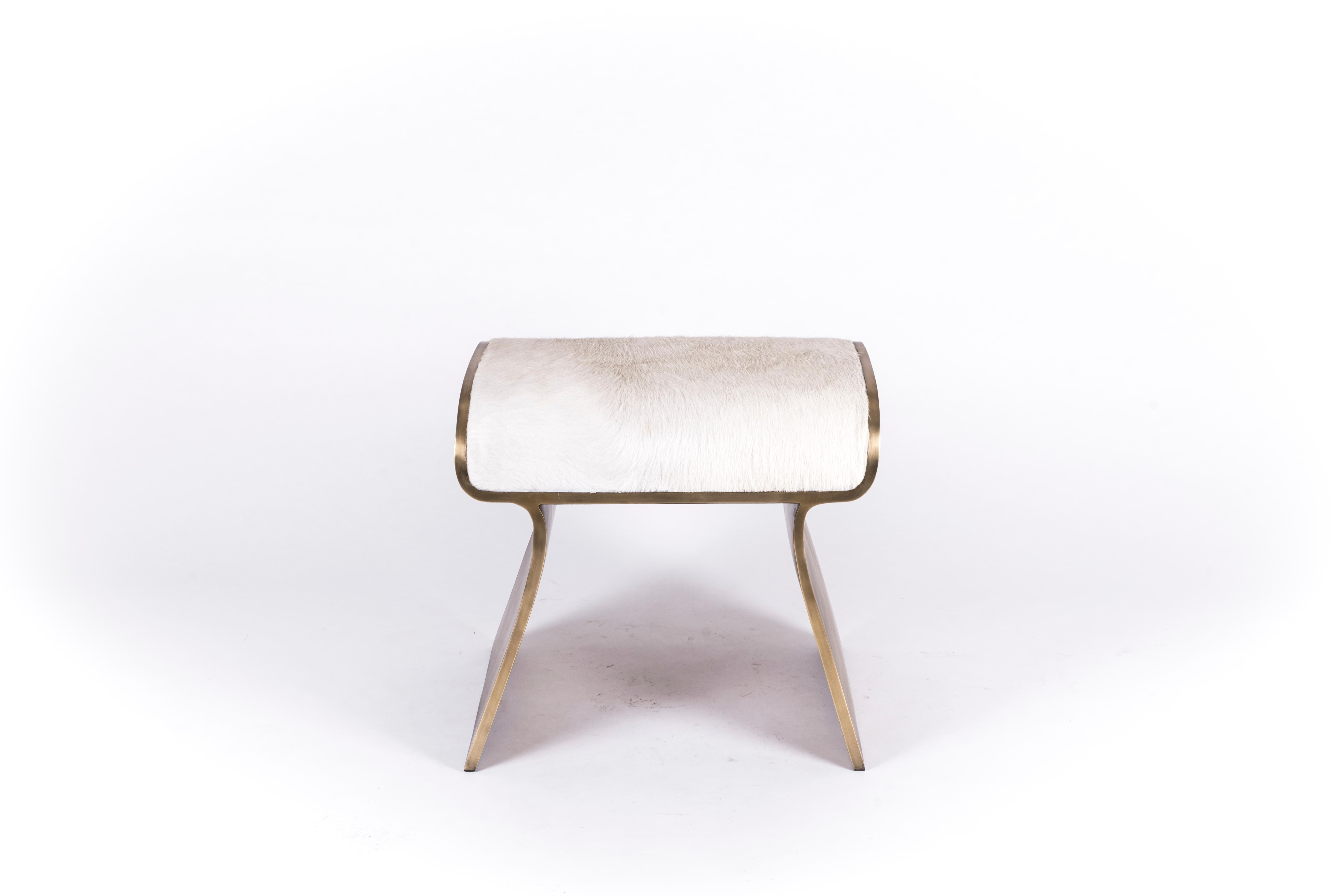 The dandy stool in upholstered in cream fur is a chic seating piece for any space. The sides of the pieces are completely inlaid in bronze-patina brass adding another luxurious element to the piece. The clean lines make it an adaptable piece and the