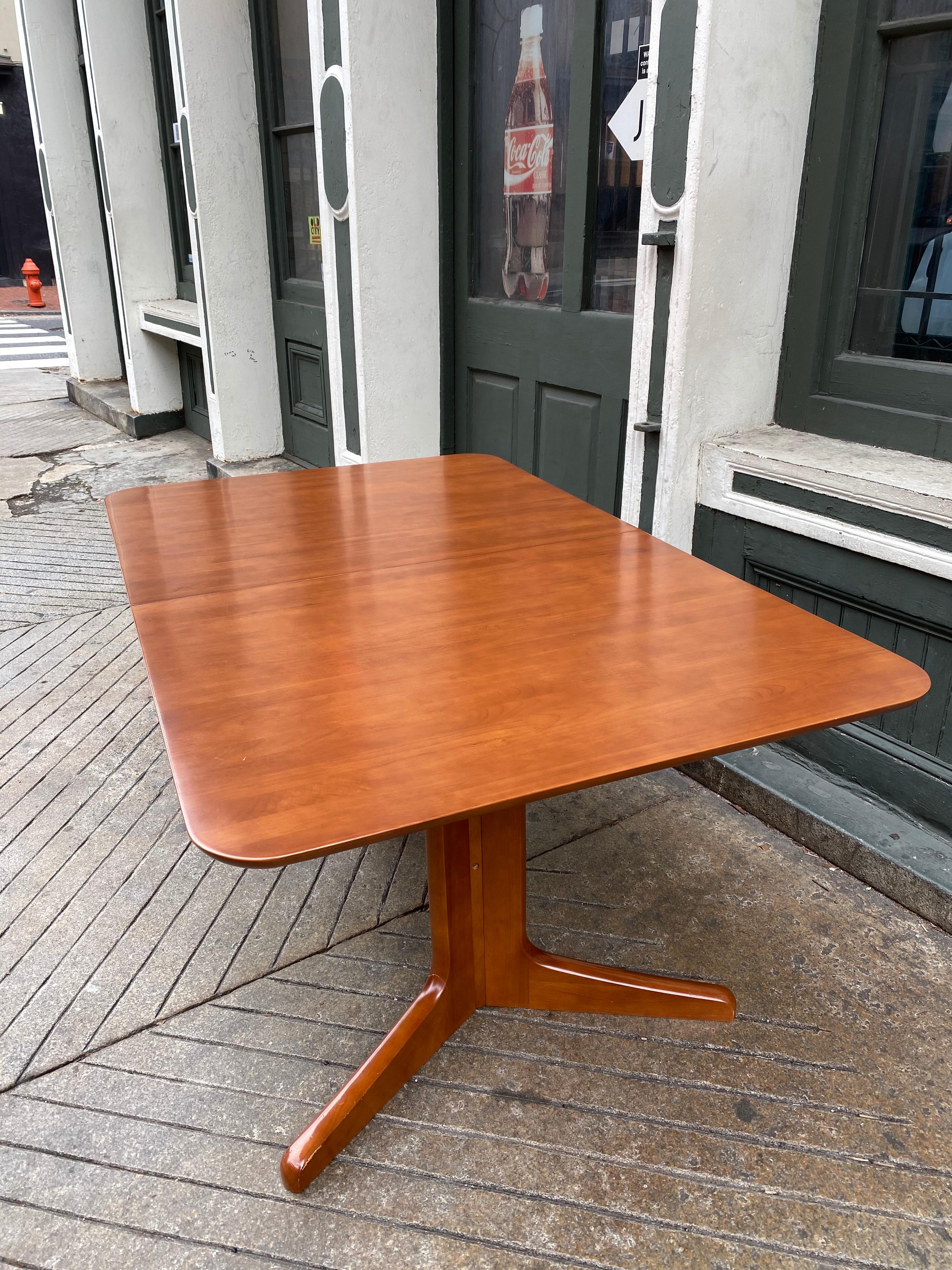 Dane decor dining table with a double pedestal design. Legs are connected with one long piece of wood. Self-storing single leaf pulls out easily. Table top has rounded corners. Color is between a cherry and teak color. One leaf measure 19.5 deep.