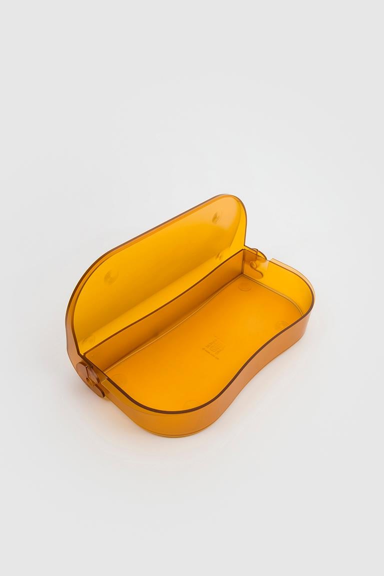 Orange Flores is a rounded, plastic pencil case. It is made up of two parts in polystyrene. The hinges are the distinctive invention of the designer and with their interlocking mechanism and simple movement represent the real ingenuity of the