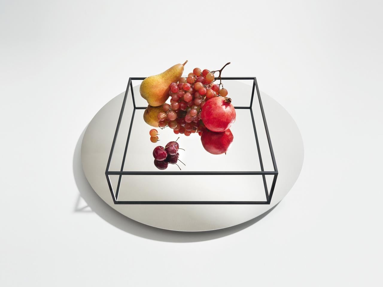 Surface e border no 1 is both a tray and a fruit bowl. The perimeter of the piece is made of thin lines of metal resting on a circular mirror. The combination of these elements creates a play of reflections that, to the eye, seems to alter the