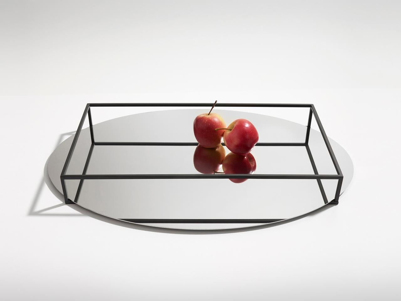 Surface e border no 2 is both a tray and a fruit bowl. The perimeter of the piece is made of thin lines of metal resting on an oval mirror. The combination of these elements creates a play of reflections that, to the eye, seems to alter the