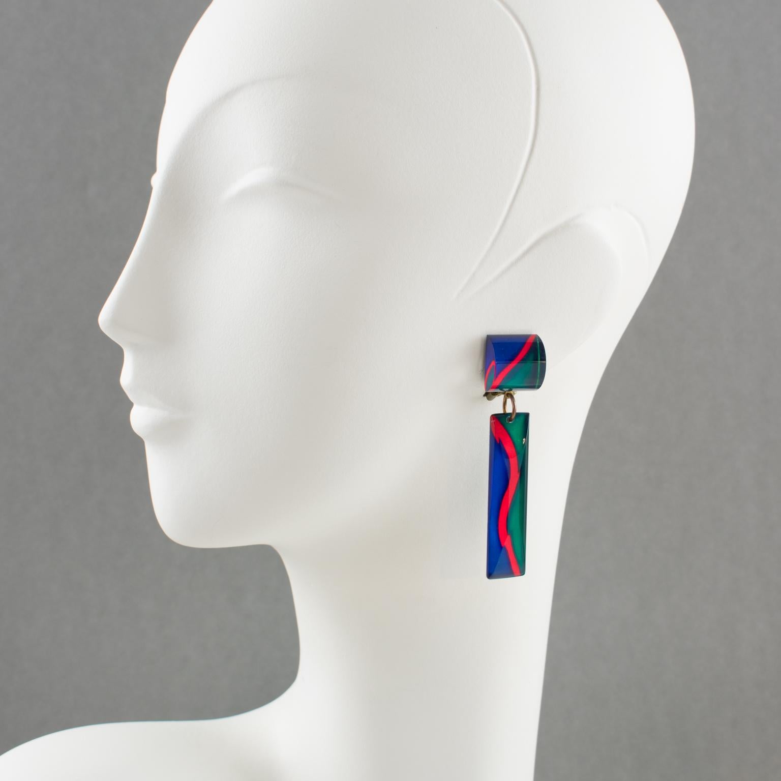 Stunning dangling Lucite clip-on earrings, featuring a geometric domed shape with an unusual zig-zag inclusion pattern. Assorted colors of electric red, cobalt blue, and bright turquoise green. No visible maker's mark.
Measurements: 2.75 in. long (7