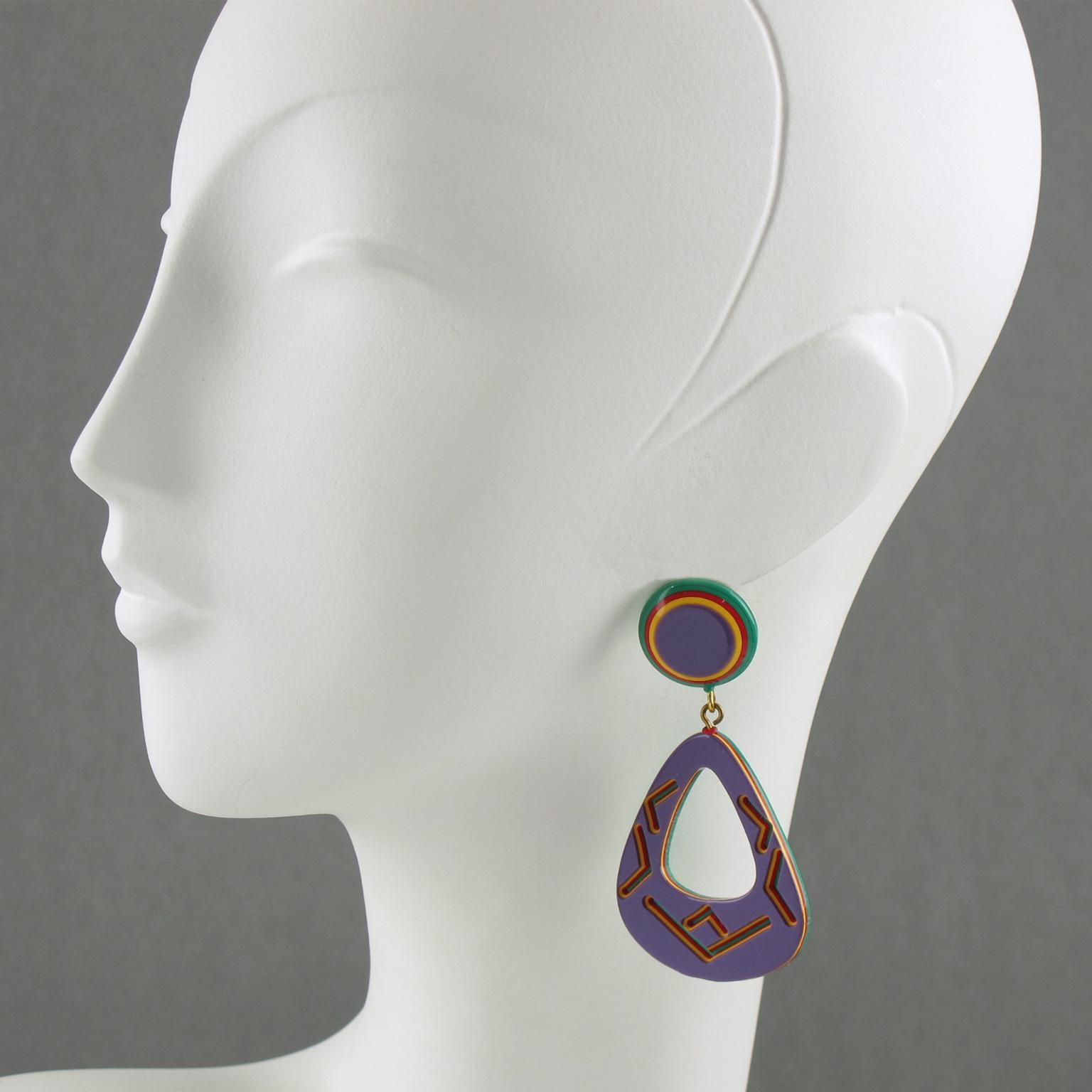These lovely Lucite earrings are for pierced ears, and they feature a dangling chandelier shape with lamination and carved tribal motifs. The pieces boast purple, red, yellow, and green colors. There is no visible maker's mark. These earrings are